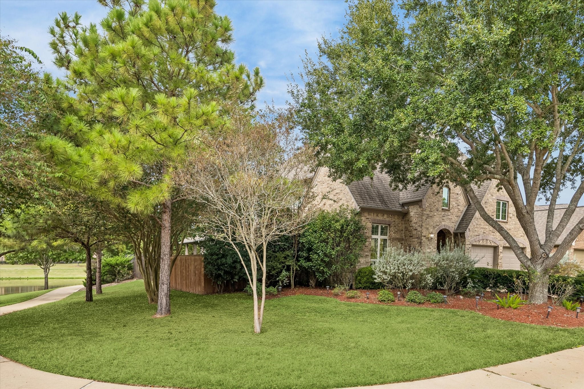 Side view highlights the home's tree-lined setting, with adjacent green space and views of the lake beyond.
