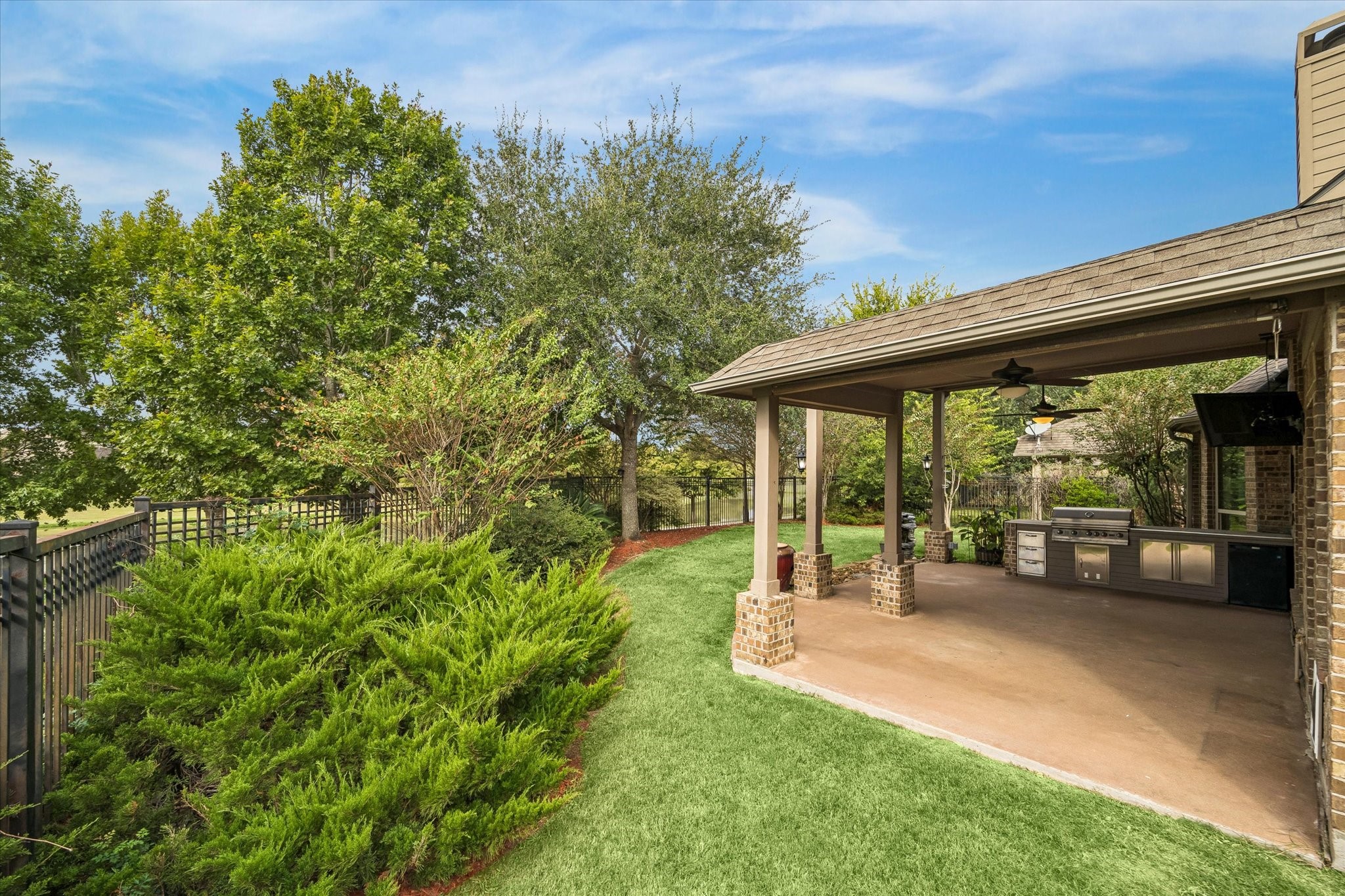 The covered patio and built-in grill invite relaxed outdoor entertaining, with lush greenery and an open setting lending a touch of country living.