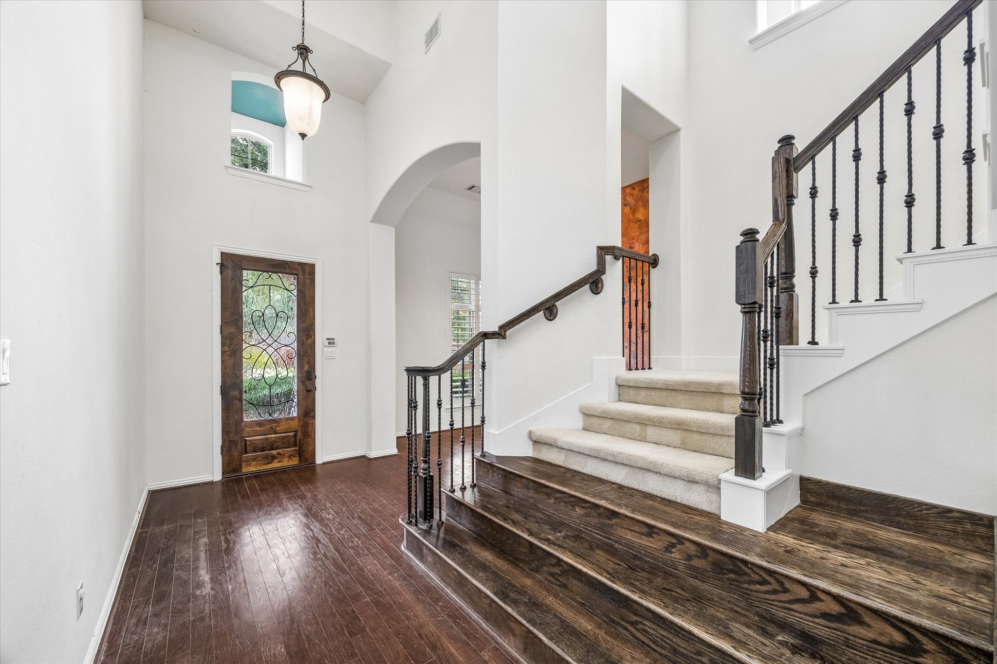 A soaring ceiling and leaded glass front door introduce the light-filled foyer, where rich wood flooring, arched openings and a staircase with iron balusters add architectural interest.