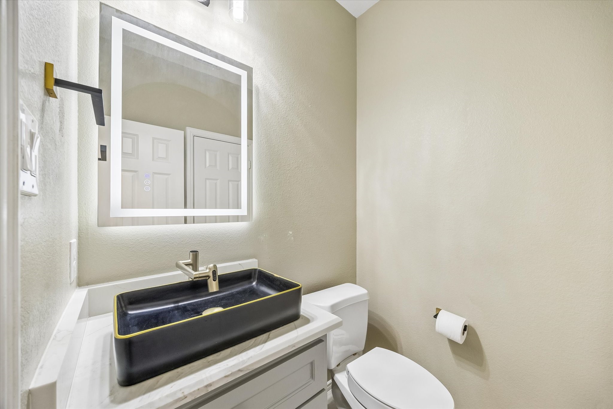 The first-floor guest powder room features a string rectangular vessel sink, an illuminated mirror and vanity with storage, combining distinctive style with everyday convenience.