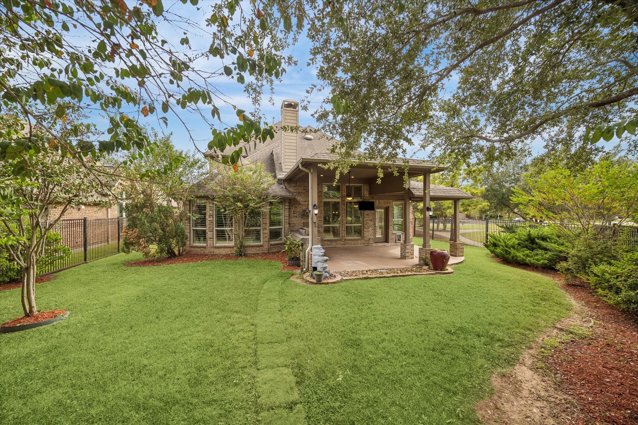 A touch of country living, with leafy tres, lush greenery, and an open lawn creating a natural retreat just beyond the covered patio.