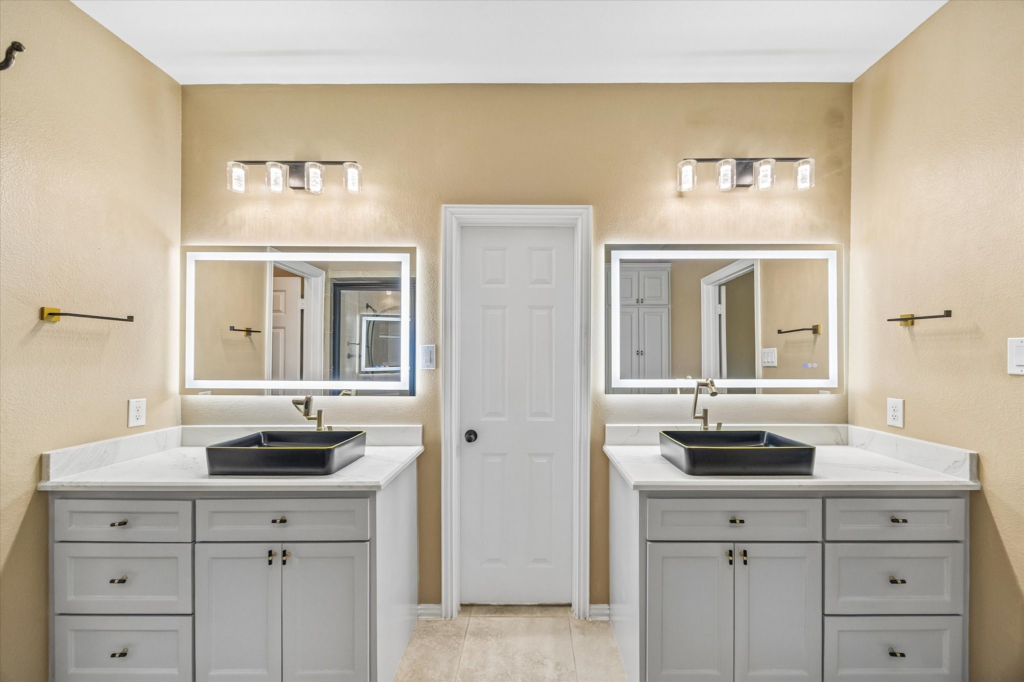 Separate vanities offer individual space, each with a rectangular vessel sink, illuminated mirror and generous drawer and cabinet storage.