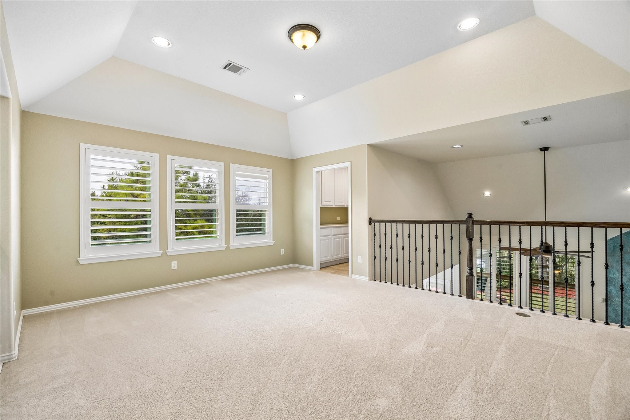 Another view of the upstairs game room highlights the raised ceiling , plantation shutters, and open railing overlooking the entry below. See entry into bar area with beverage refrigerator.