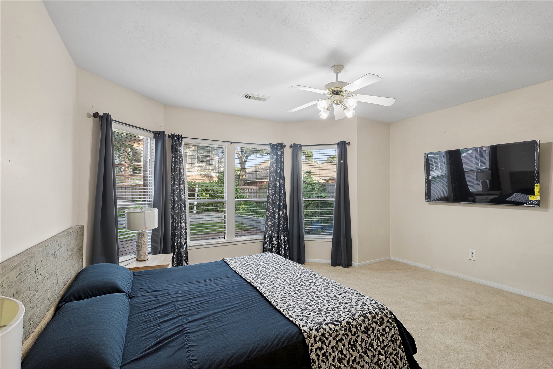 This spacious bedroom features large bay windows with abundant natural light, neutral walls, and carpet flooring.