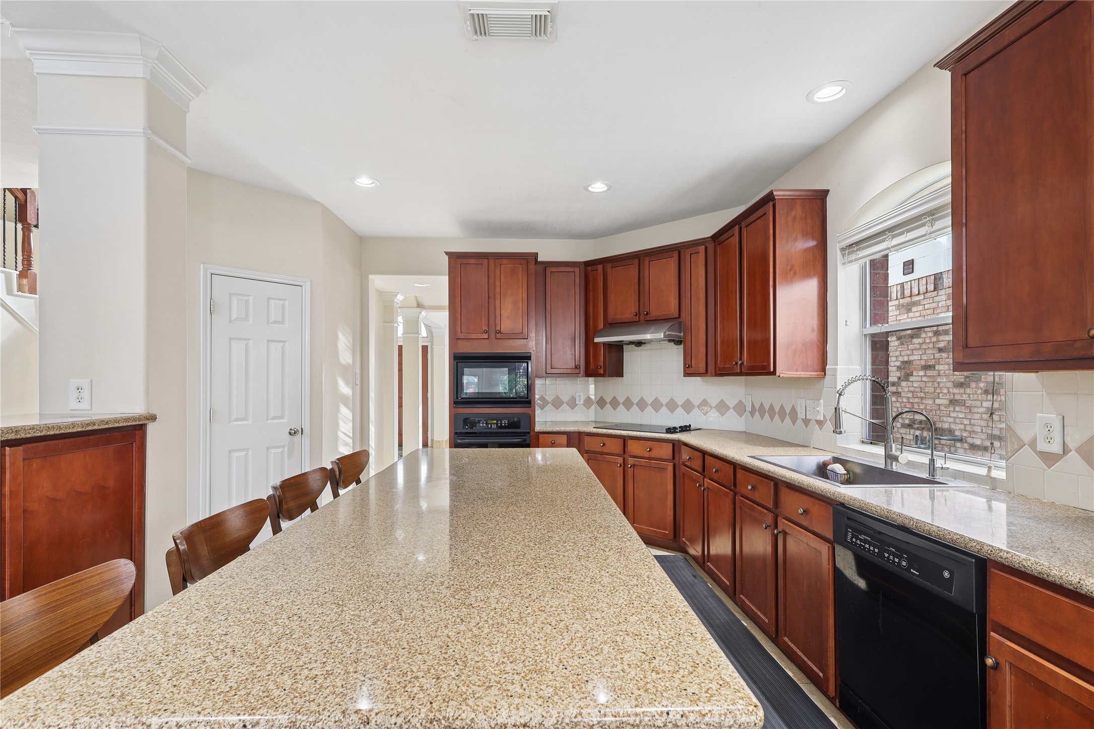 This spacious kitchen features elegant wood cabinetry, a large granite island with seating, and modern appliances, offering a bright and functional space for cooking and entertaining.