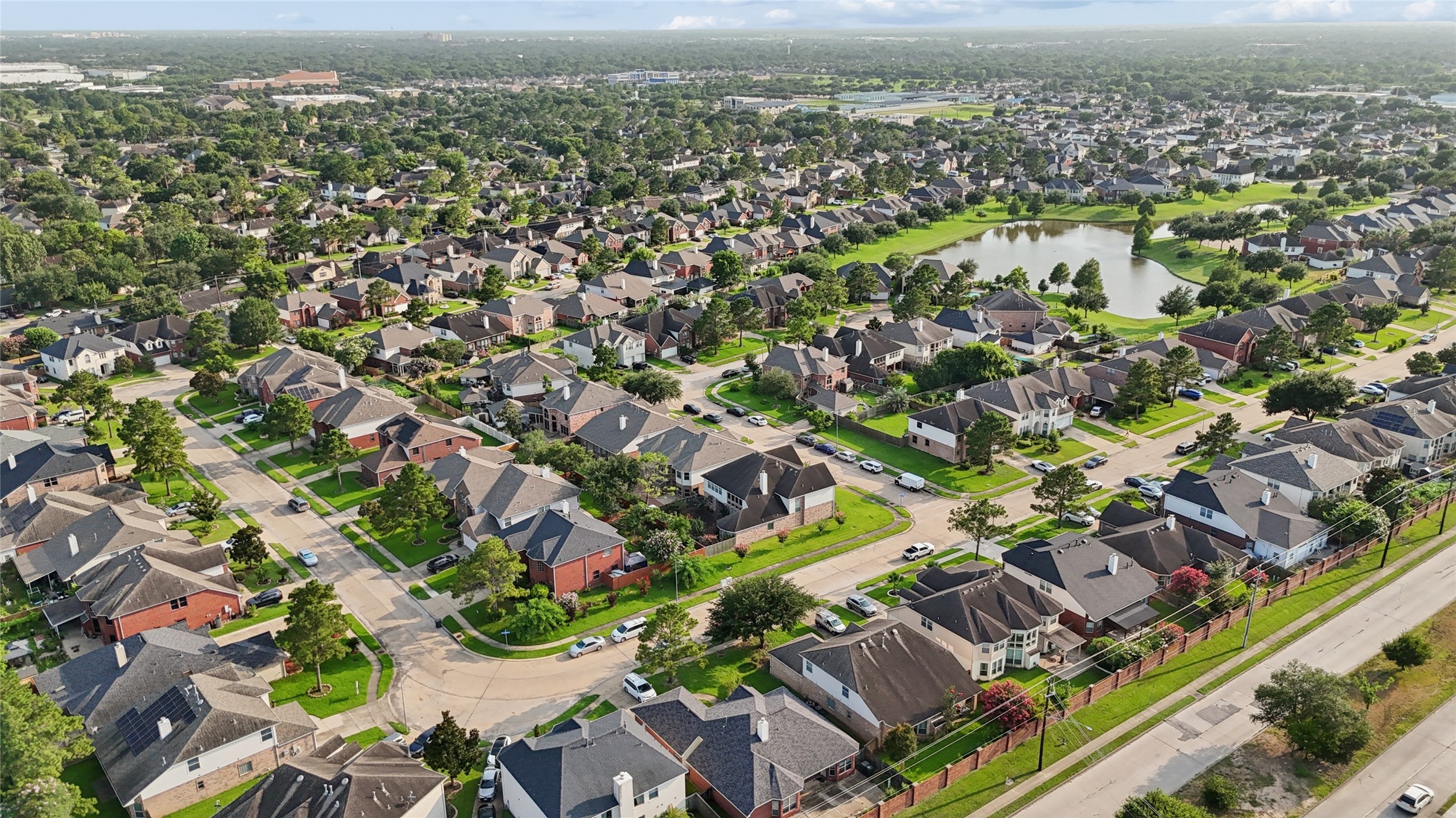 This aerial photo showcases a sprawling suburban neighborhood with well-maintained homes, tree-lined streets, and a nearby pond. The area appears peaceful and family-friendly, with convenient access to amenities and green spaces.