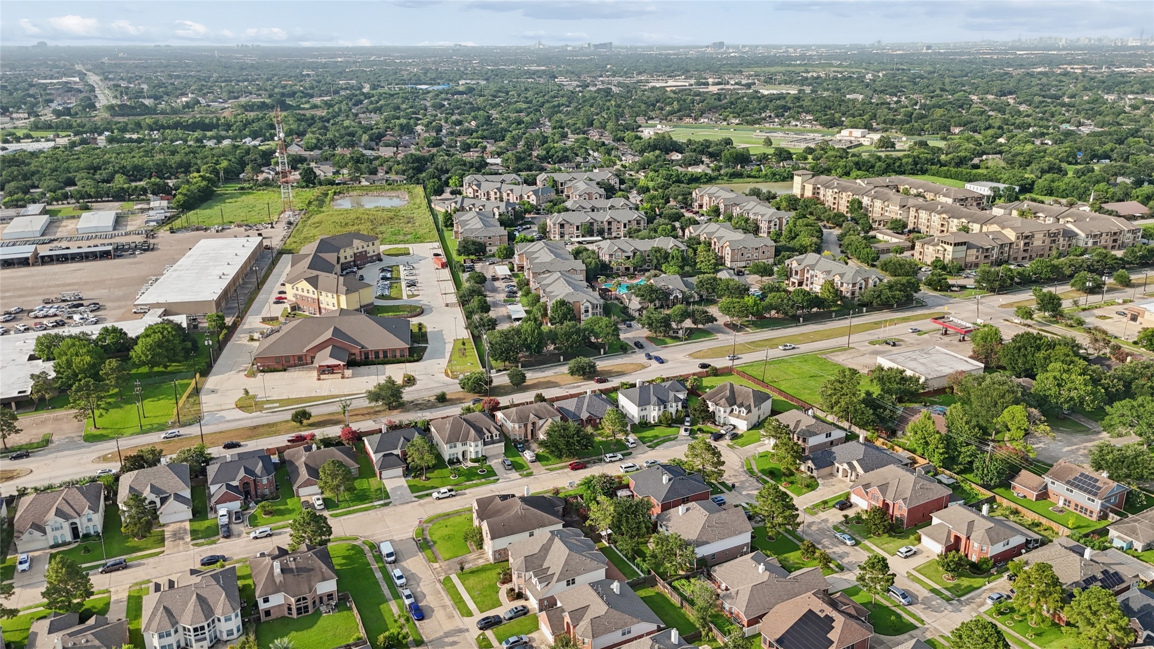 This aerial photo showcases a suburban neighborhood with well-maintained single-family homes, tree-lined streets, and nearby commercial buildings. The area appears spacious and green, offering a mix of residential and commercial conveniences.