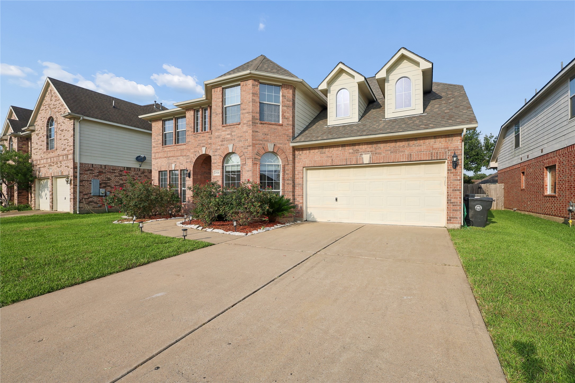 This photo showcases a two-story brick home with a well-maintained lawn, a double garage, and charming dormer windows. The driveway is spacious, and the front garden features attractive landscaping. Perfect for a family seeking a suburban setting. This photo showcases a two-story brick home with a well-maintained lawn, a double garage, and charming dormer windows. The driveway is spacious, and the front garden features attractive landscaping. Perfect for a family seeking a suburban setting.
