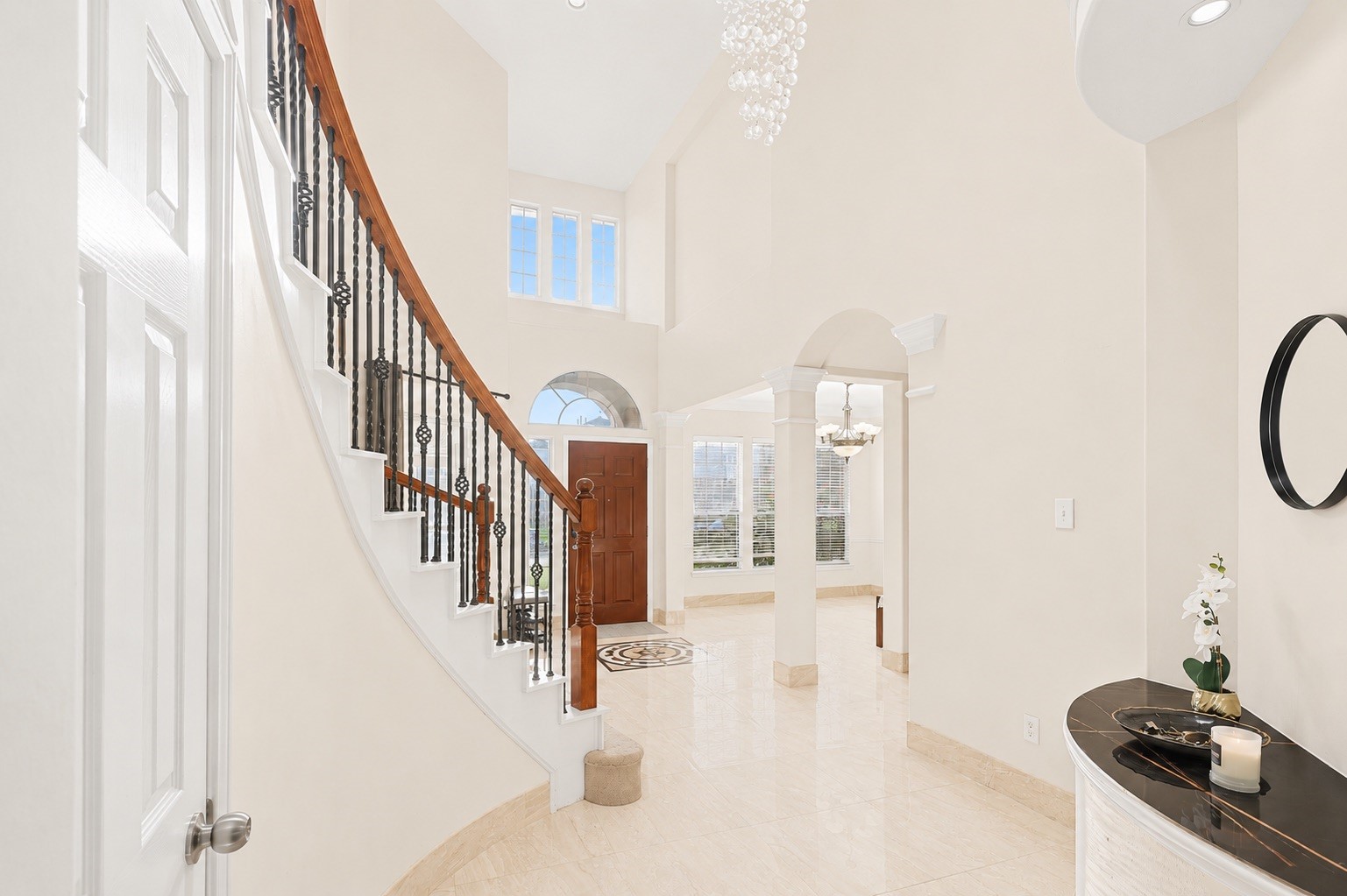 Bright and elegant foyer with a grand curved staircase, high ceilings, and large windows. The space features polished floors, a stylish chandelier, and an inviting entrance that leads to an open living area. Bright and elegant foyer with a grand curved staircase, high ceilings, and large windows. The space features polished floors, a stylish chandelier, and an inviting entrance that leads to an open living area.