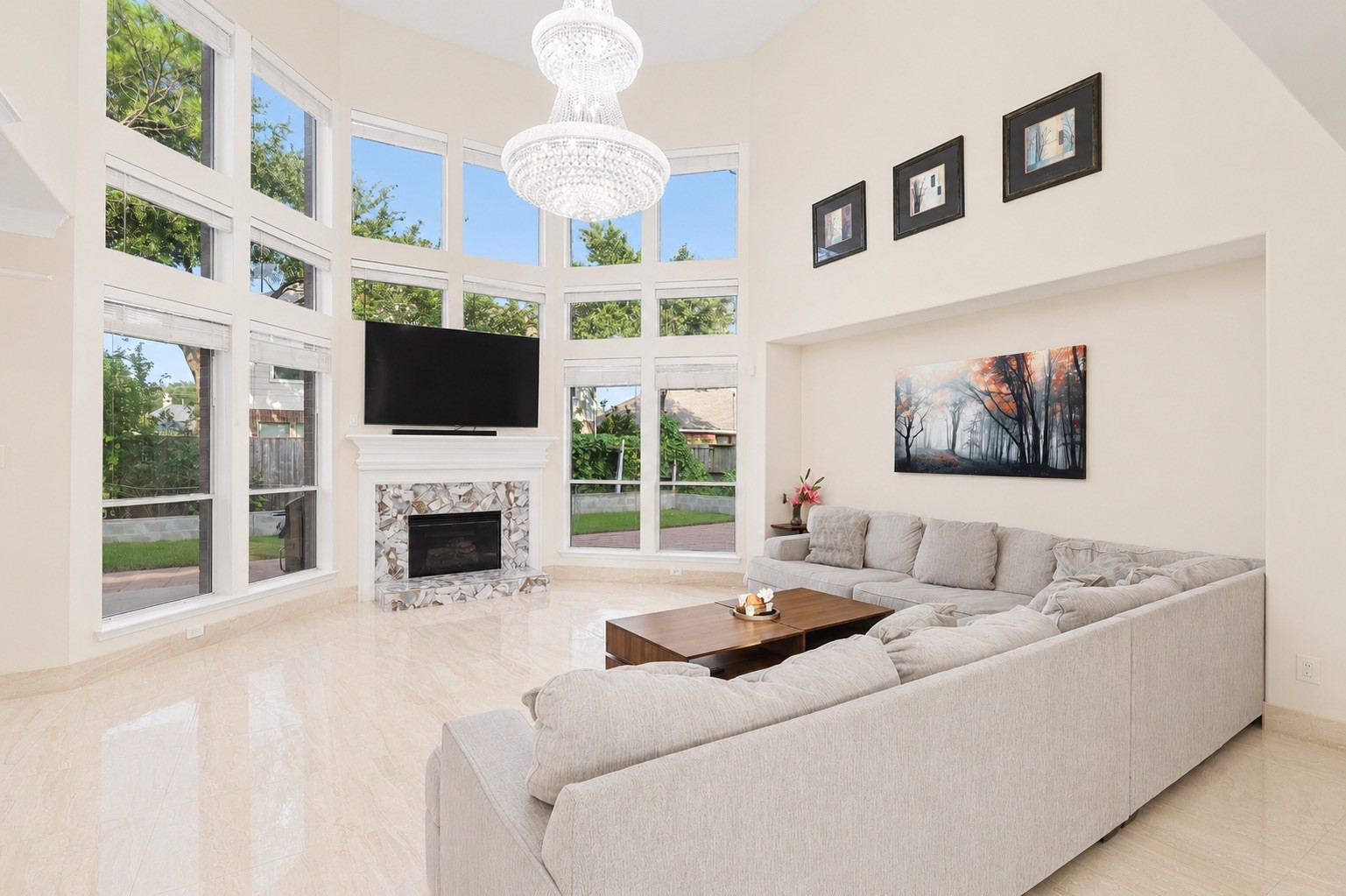 Spacious living room with high ceilings and large windows providing abundant natural light. Features a modern chandelier, a cozy fireplace.