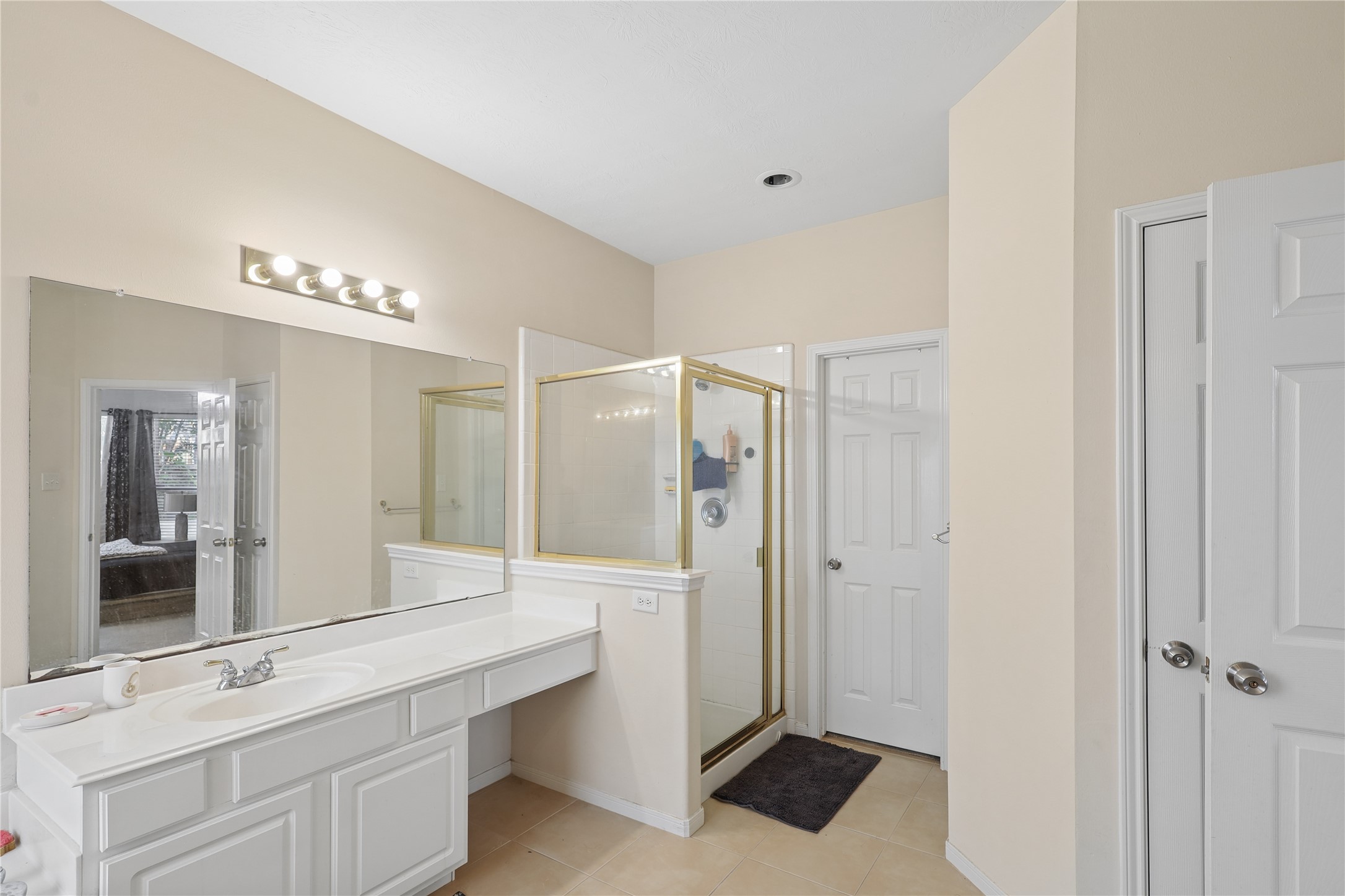 Bright, spacious bathroom with a large mirror, ample counter space, and a glass-enclosed shower. Neutral tones create a clean, modern look.