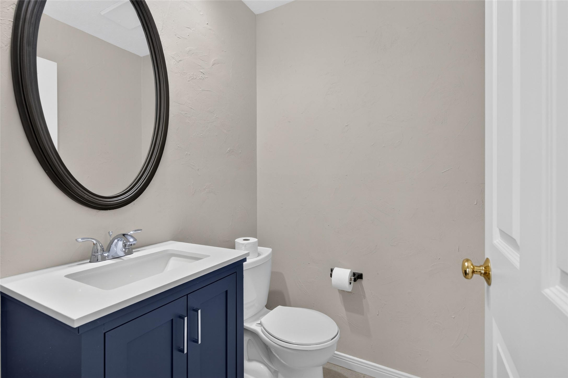 A stylish navy vanity, modern fixtures, and a circular mirror add personality to this conveniently located half bath while keeping the space polished and functional.