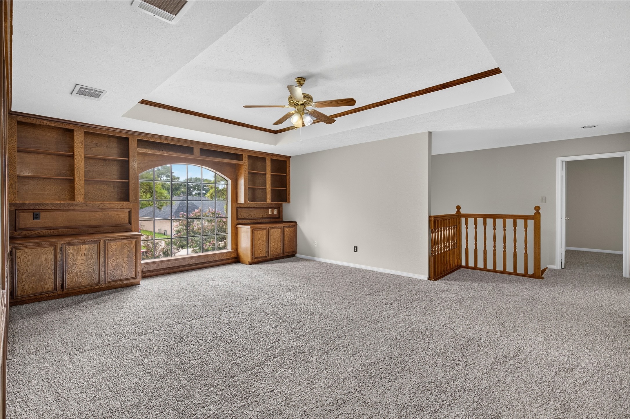 Plush carpeting, built-in wood shelving, and a large arched window create a bright, flexible room with plenty of character and natural light.