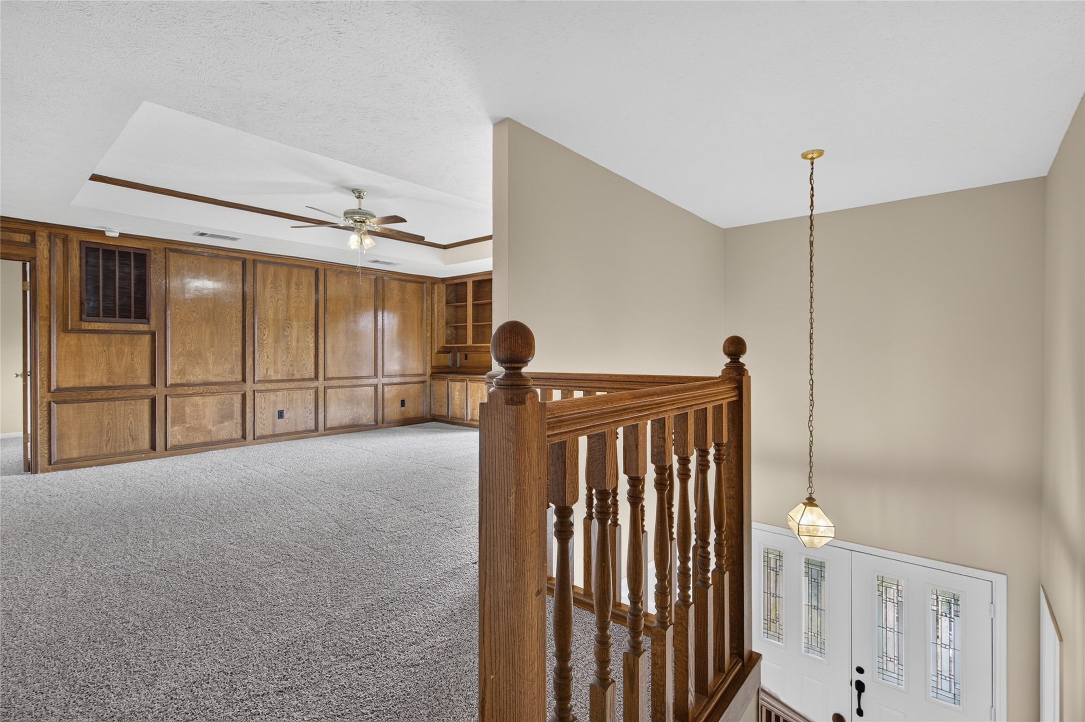Wood paneling, a ceiling fan, and a view toward the bright entryway create a distinctive upper-level transition space with architectural character and an open sense of connection.