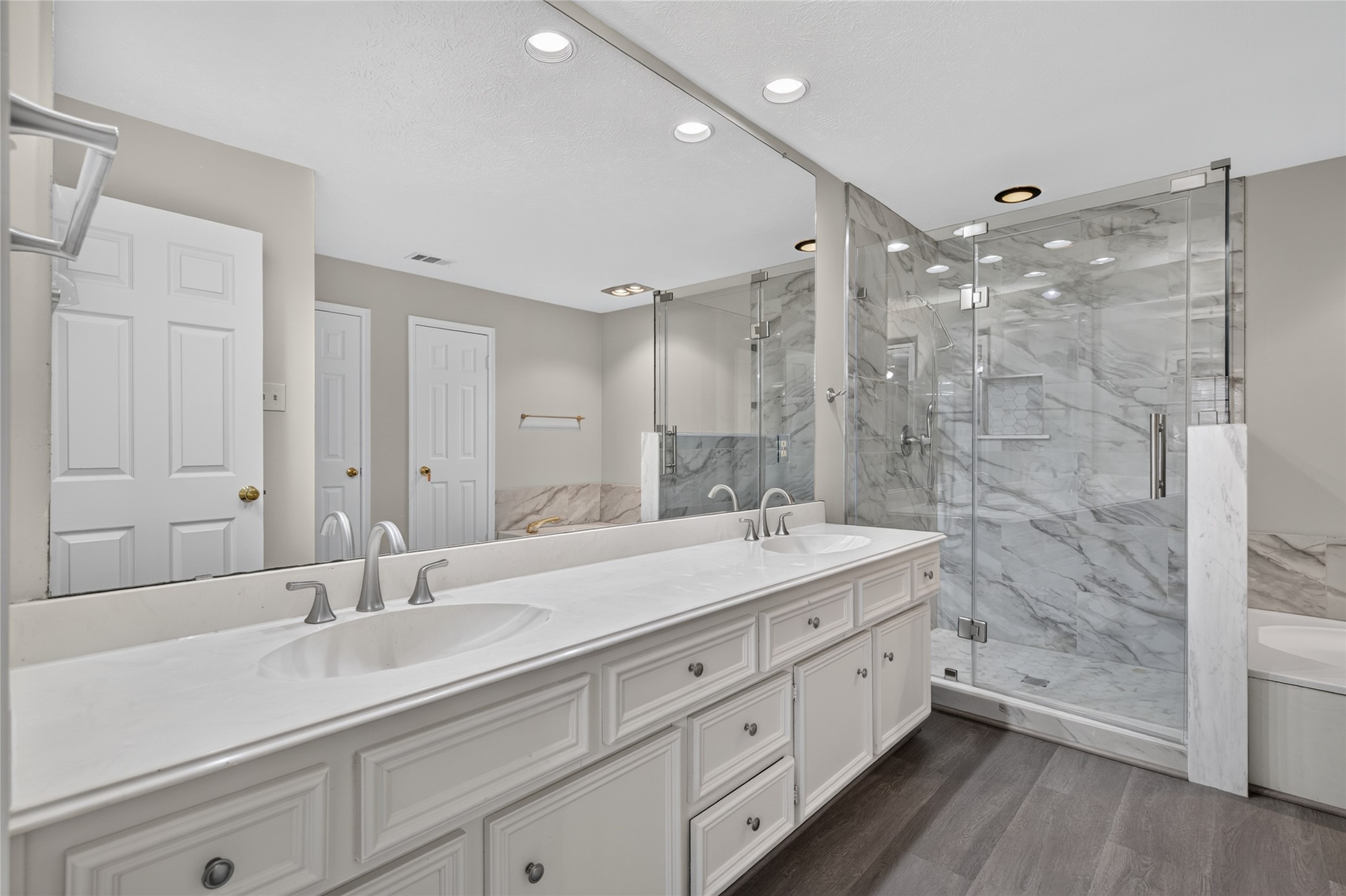 A spacious double vanity, marble countertops, and a glass-enclosed shower create a polished bathroom setting with the feel of a private retreat.