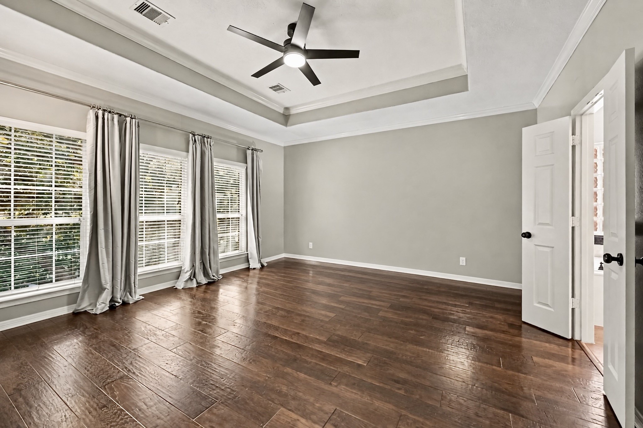 Expansive bedroom with tray ceiling, wood flooring, and a wall of windows.Virtually unstaged to highlight the rooms size and versatility.