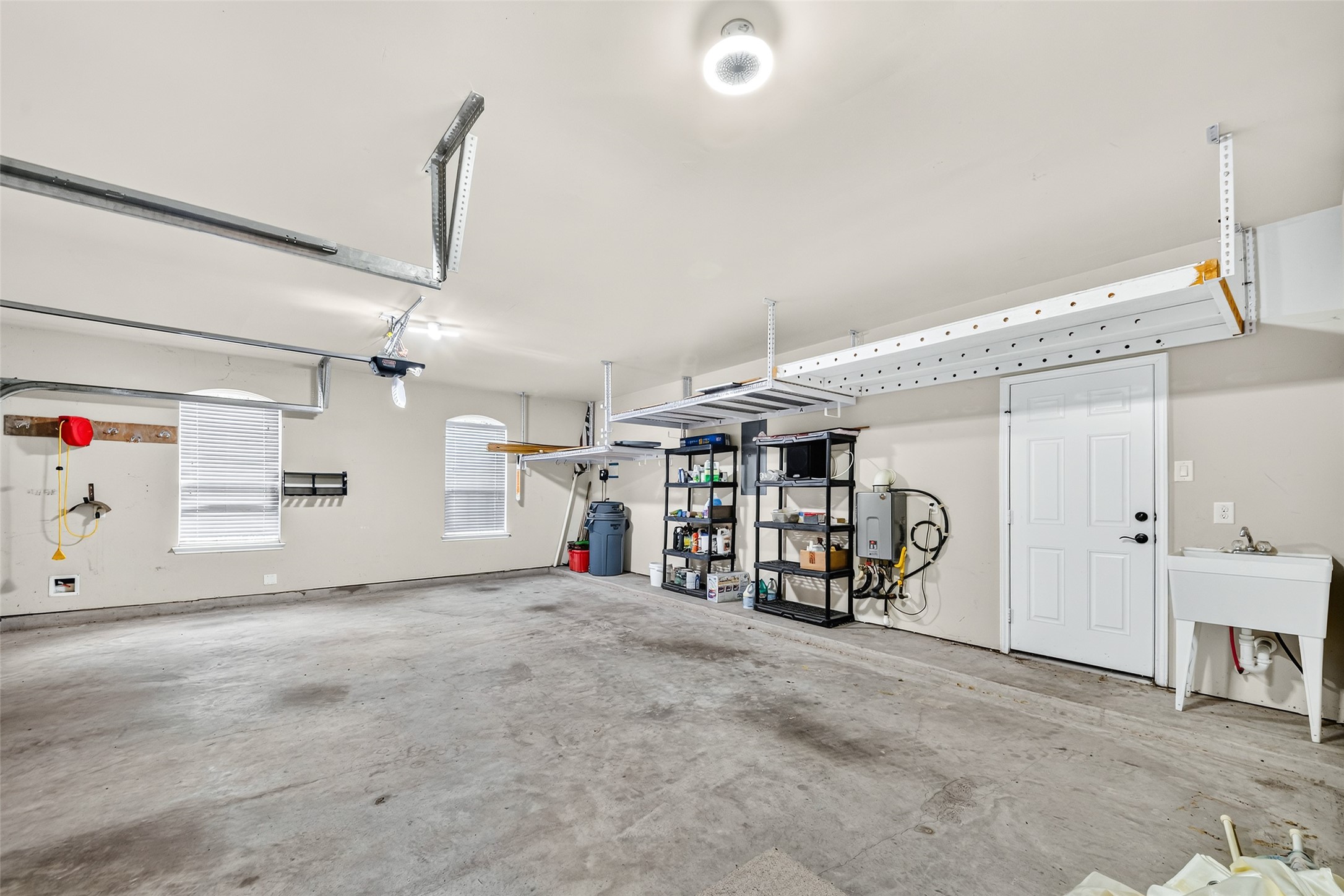Spacious 3-car garage with ample storage solutions, featuring overhead racks, shelving units, and a convenient utility sink.