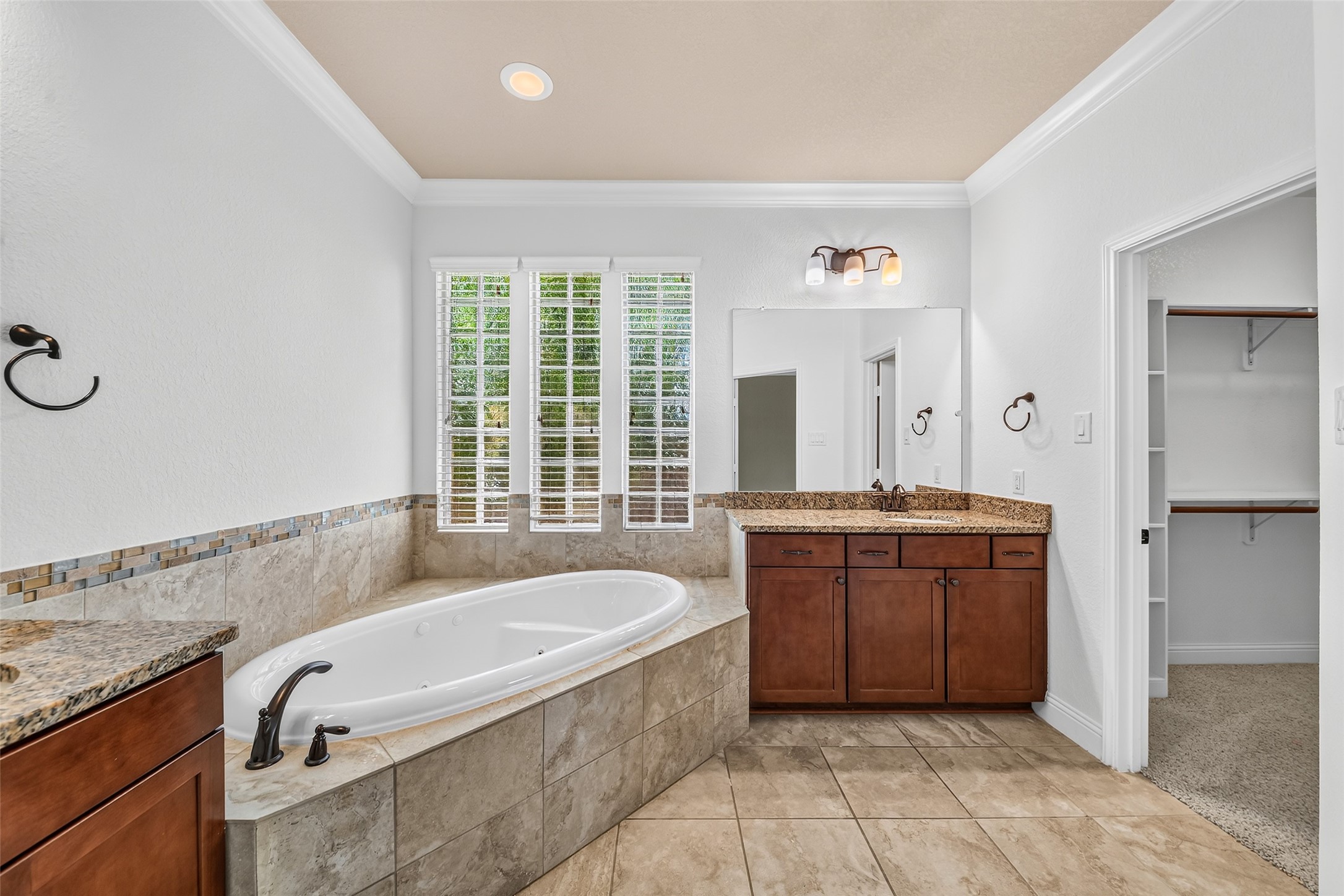 Elegant primary bathroom featuring a luxurious corner tub, dual sinks with granite countertops.