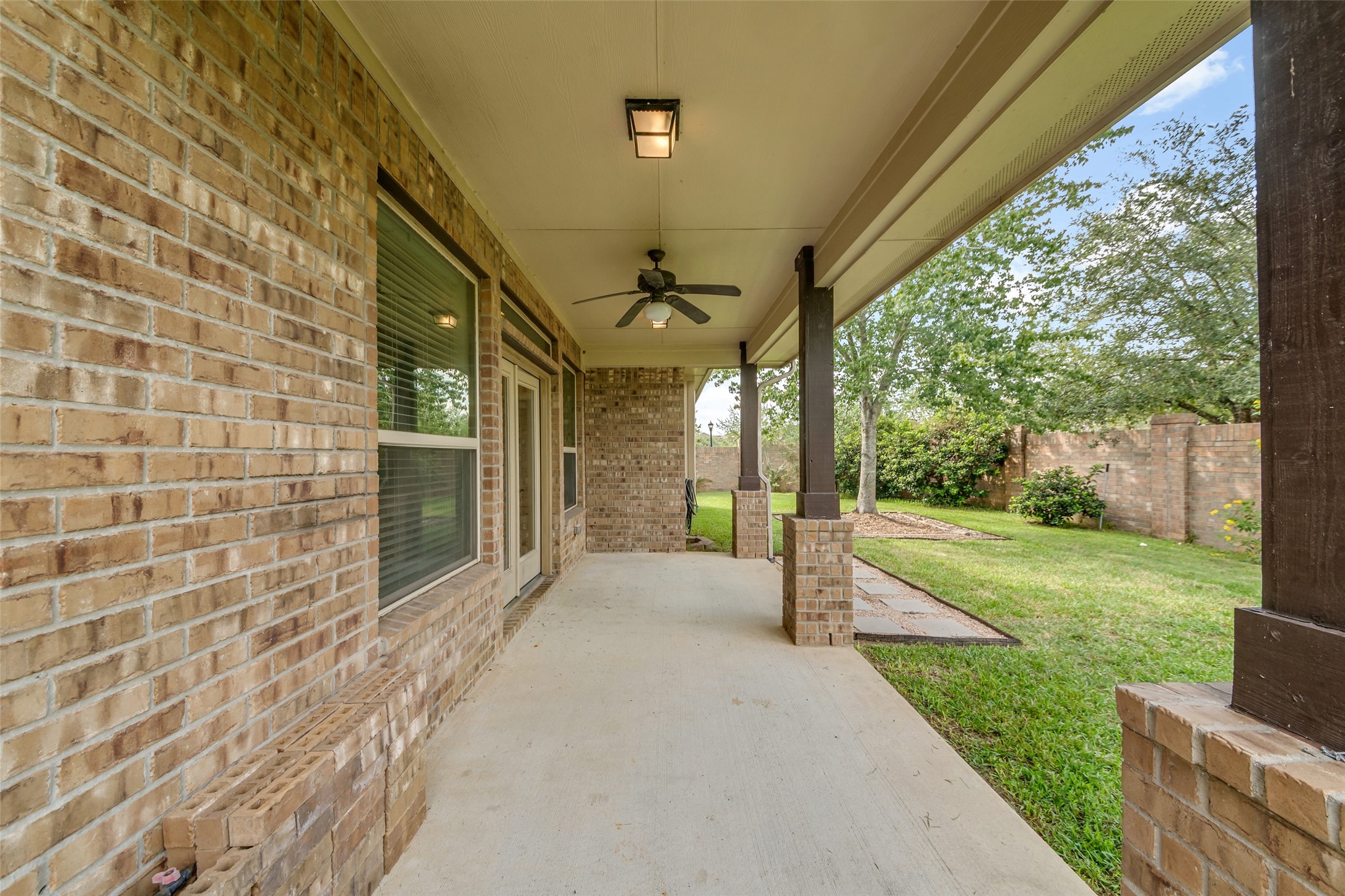 Spacious covered patio with a ceiling fan and brick accents.