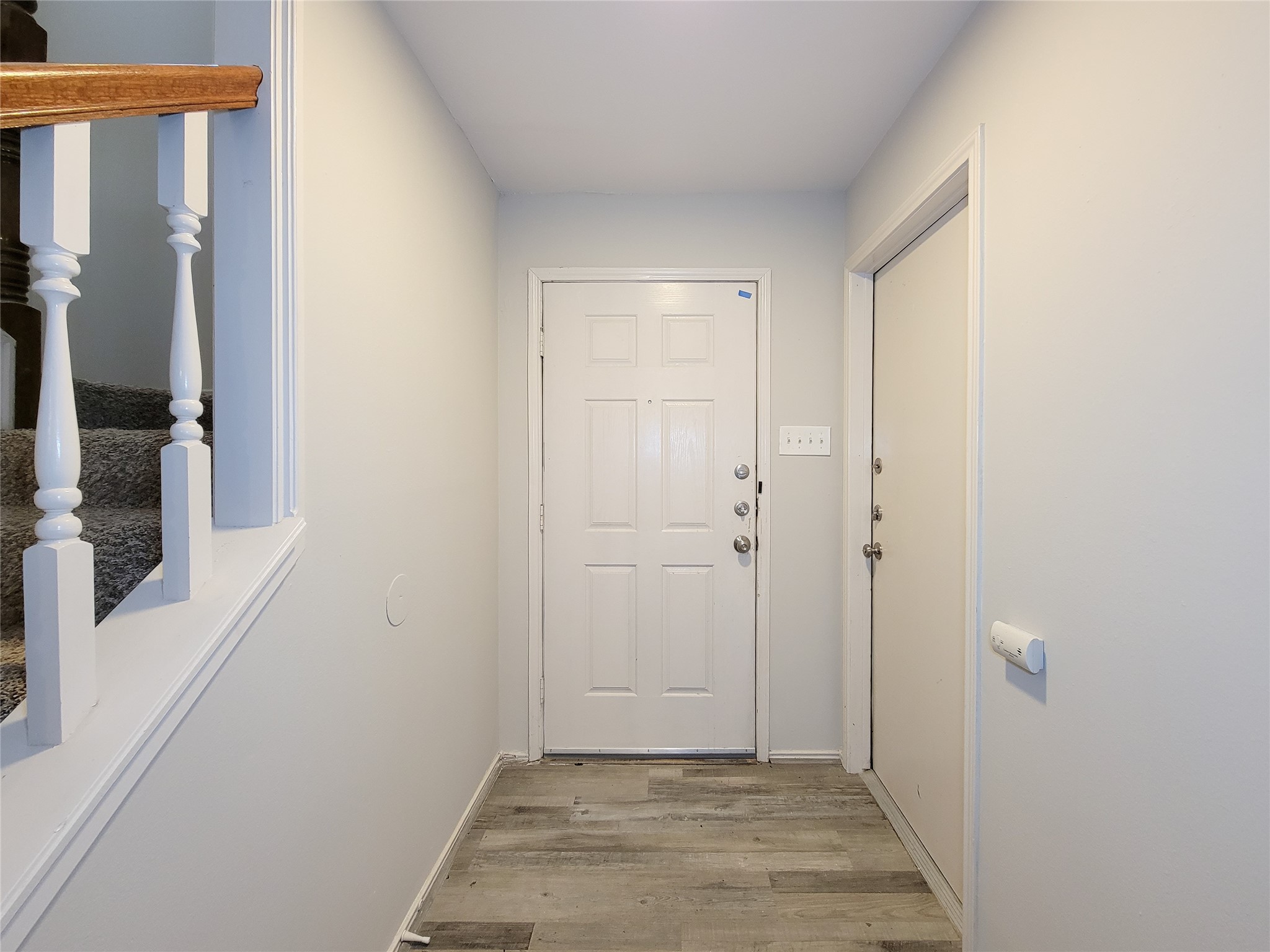 Inviting entryway with a modern white door, stylish wood-look flooring, and a staircase featuring classic balustrades.