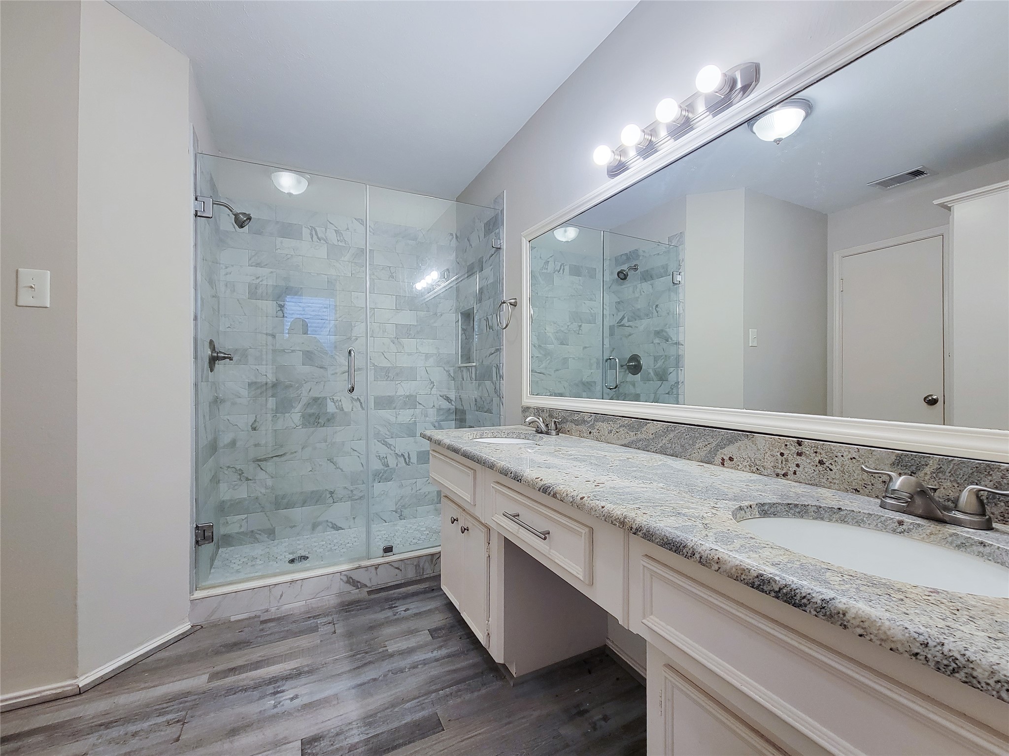 Elegant bathroom featuring a spacious glass-enclosed shower with stylish tiled walls, a sleek dual-sink vanity with granite countertops, and modern lighting fixtures.