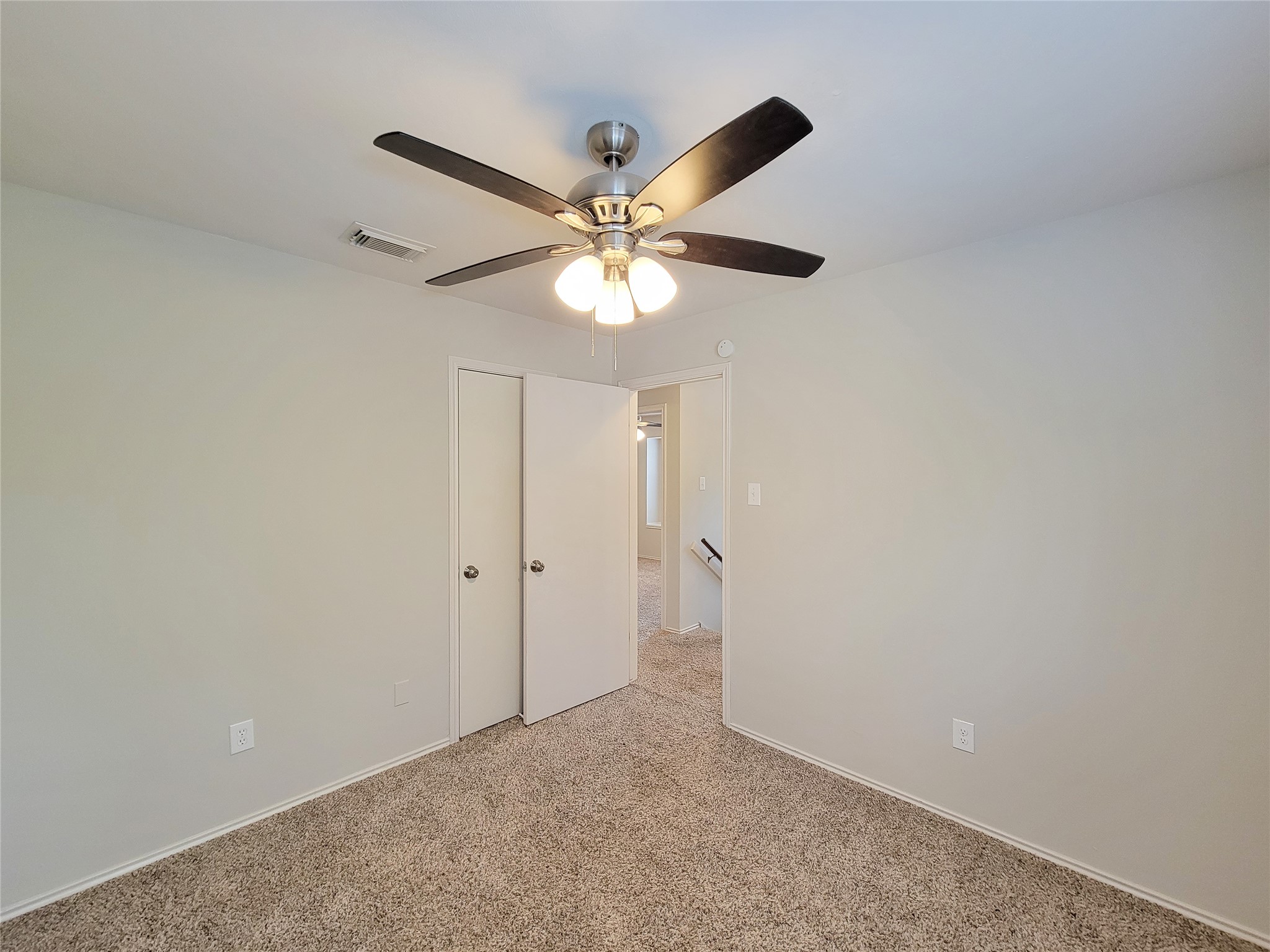Bright and inviting bedroom with plush carpeting, featuring a modern ceiling fan and ample natural light.