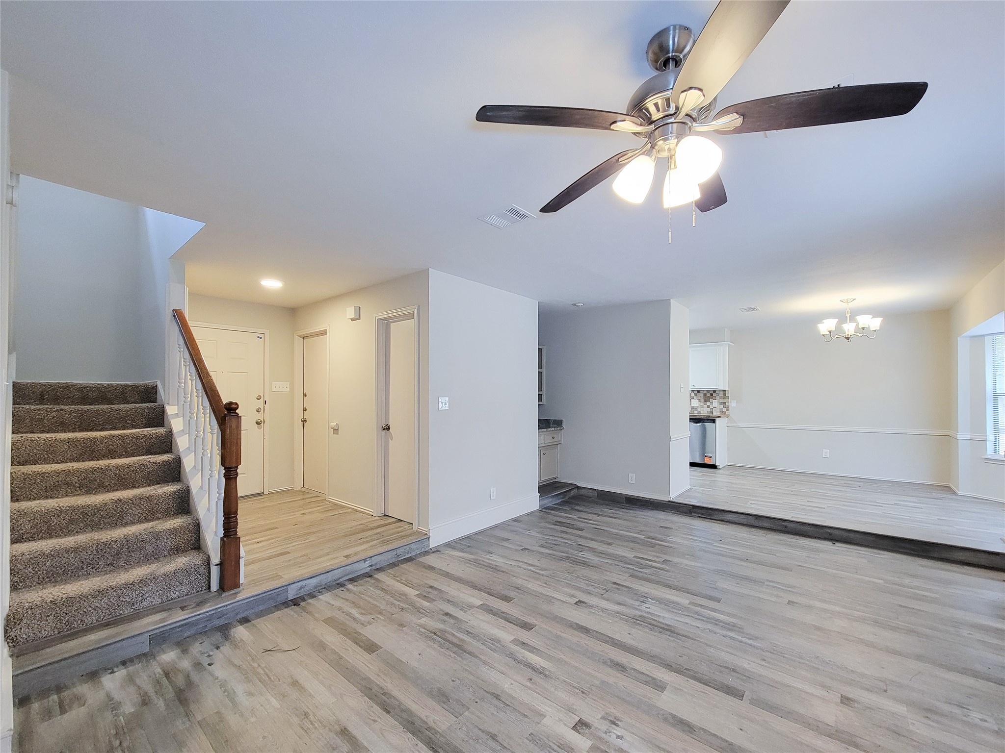 Spacious open-plan living area with elegant laminate flooring, modern ceiling fan, and a cozy carpeted staircase leading to the upper level.