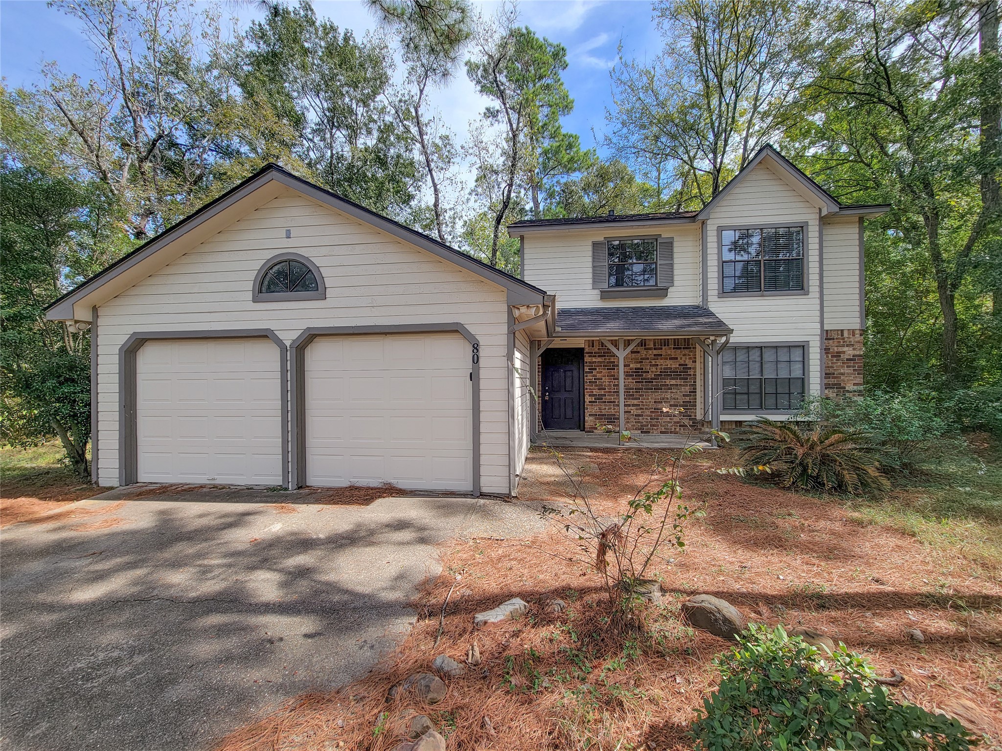 Charming two-story home with a spacious two-car garage, surrounded by lush greenery and nestled in a serene wooded setting.