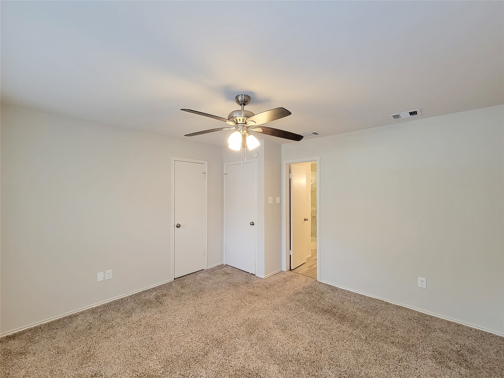 Spacious bedroom featuring plush carpeting, a ceiling fan for comfort, and a convenient en-suite bathroom.