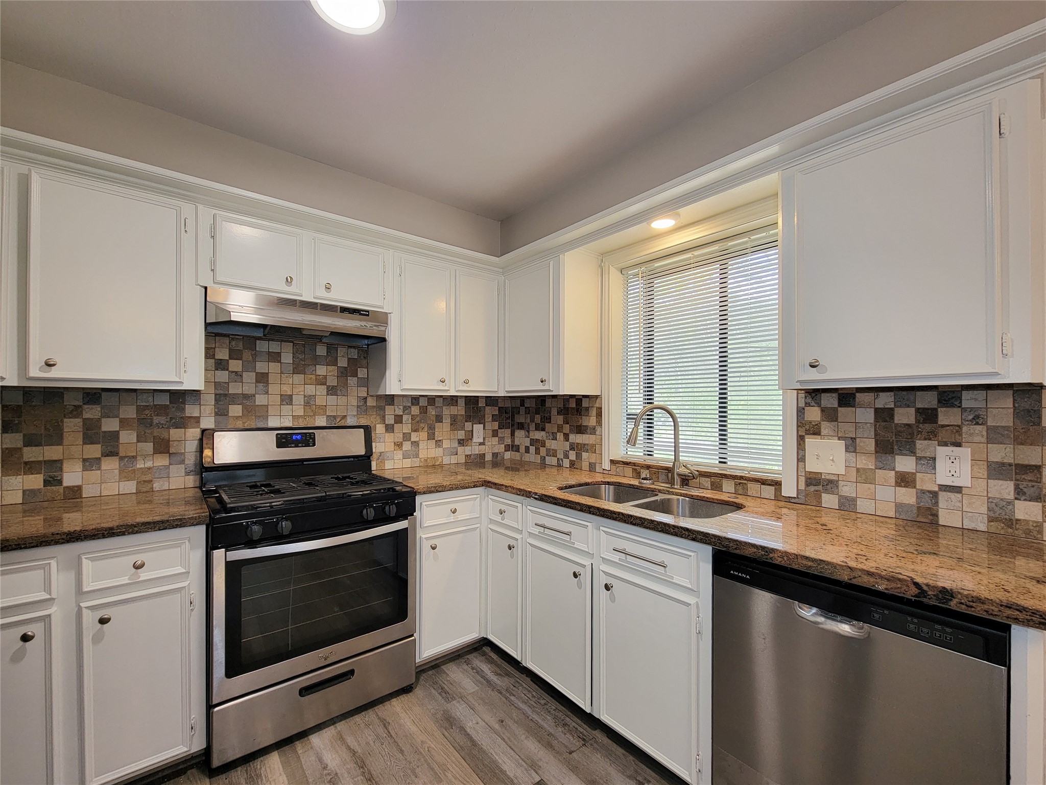 Modern kitchen with stainless steel appliances, elegant granite countertops, and a stylish tiled backsplash, complemented by ample white cabinetry and a double sink.