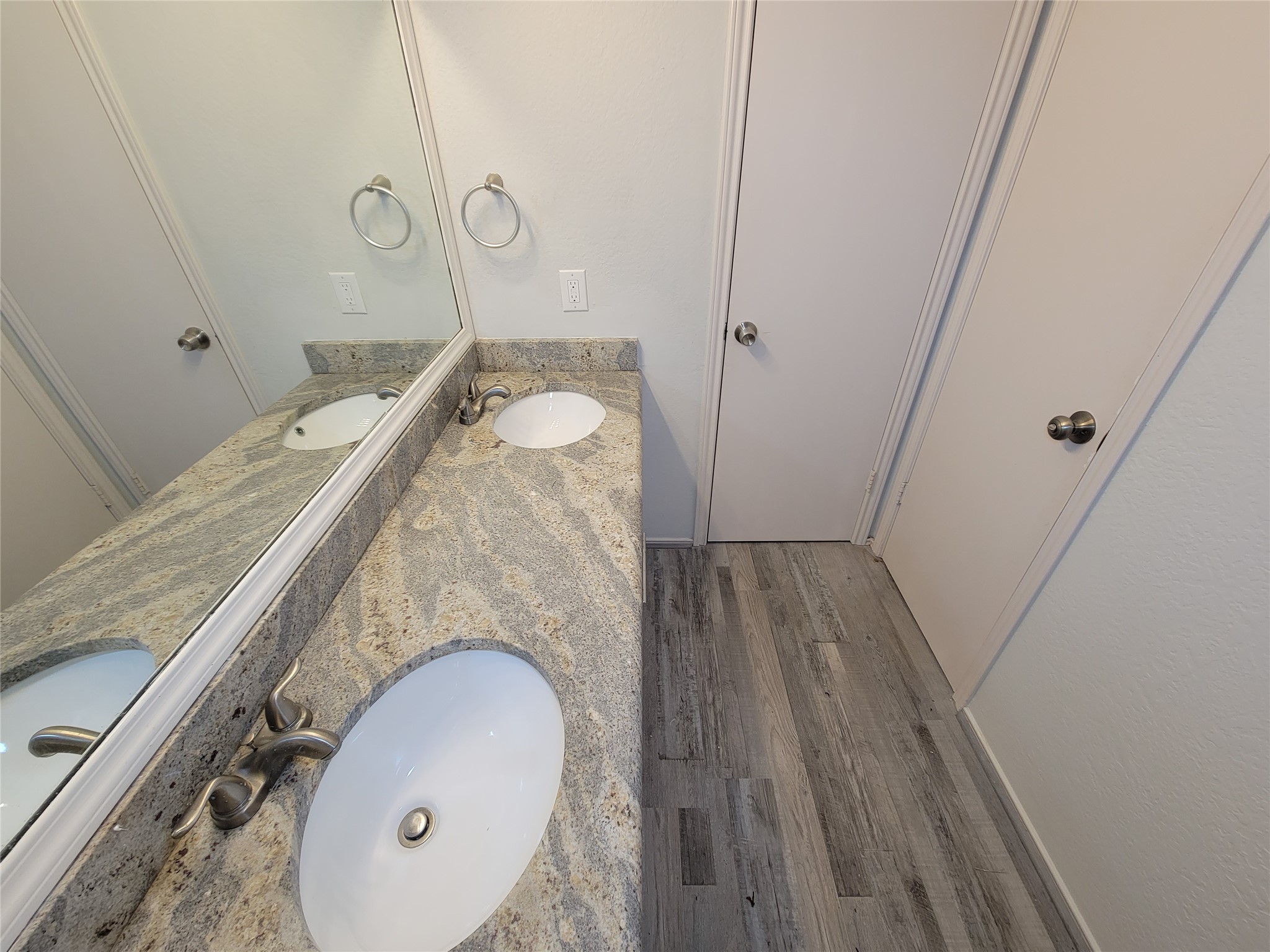 Elegant bathroom featuring a dual-sink vanity with granite countertops and stylish fixtures, complemented by sleek flooring and ample mirror space.