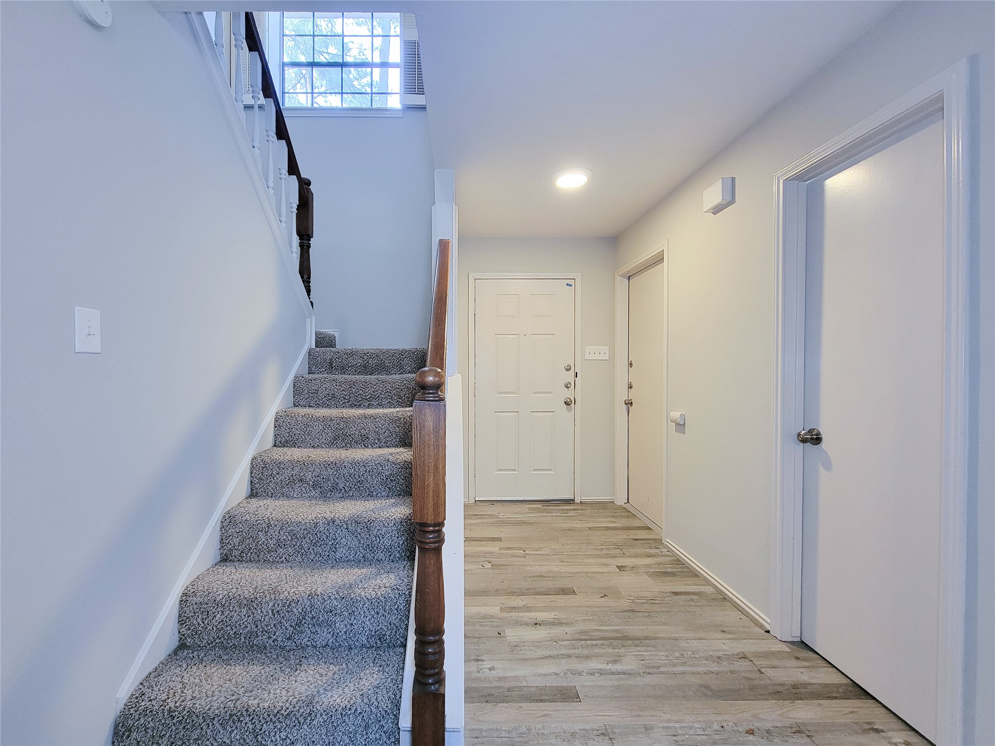 Bright and welcoming entryway with modern flooring and a carpeted staircase leading to the upper level, complemented by neutral walls for a fresh, airy feel.