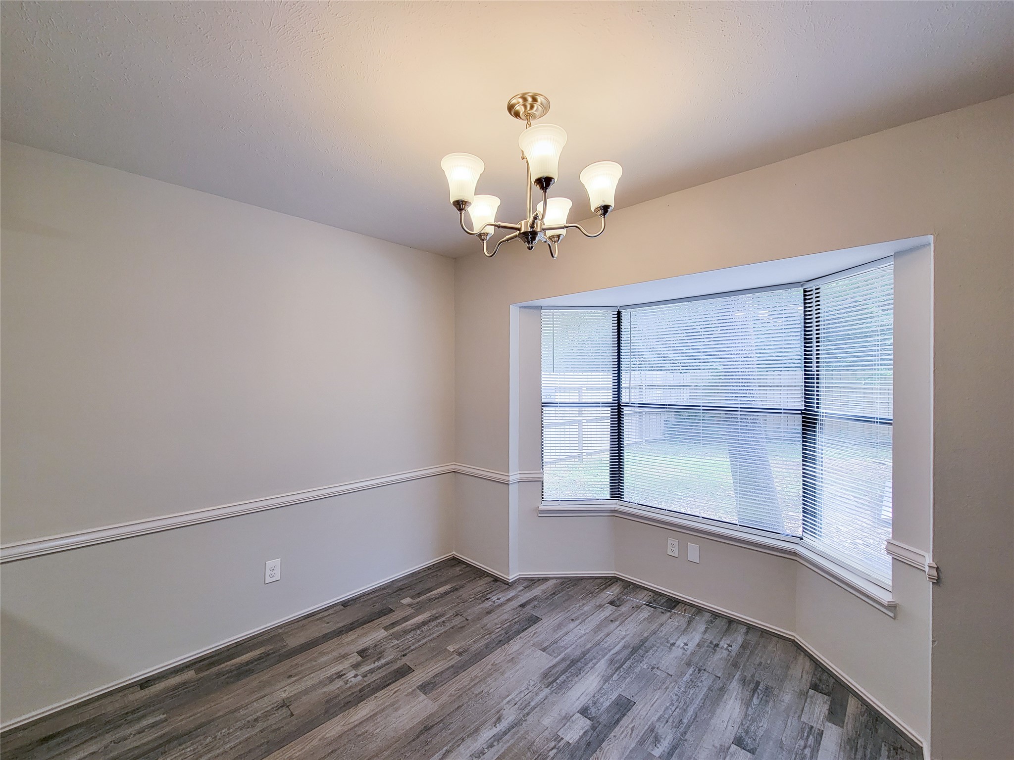 Bright dining area featuring a stylish chandelier, elegant wainscoting, and a large bay window offering natural light and views of the backyard.