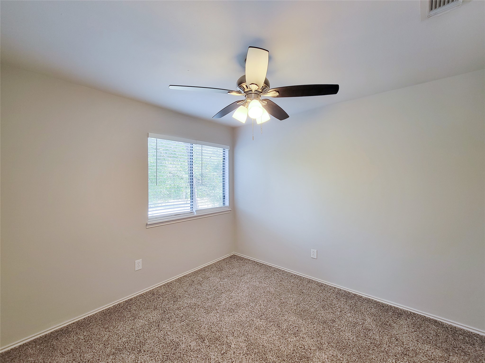 Cozy bedroom with plush carpeting, featuring a ceiling fan and natural light streaming through a large window.