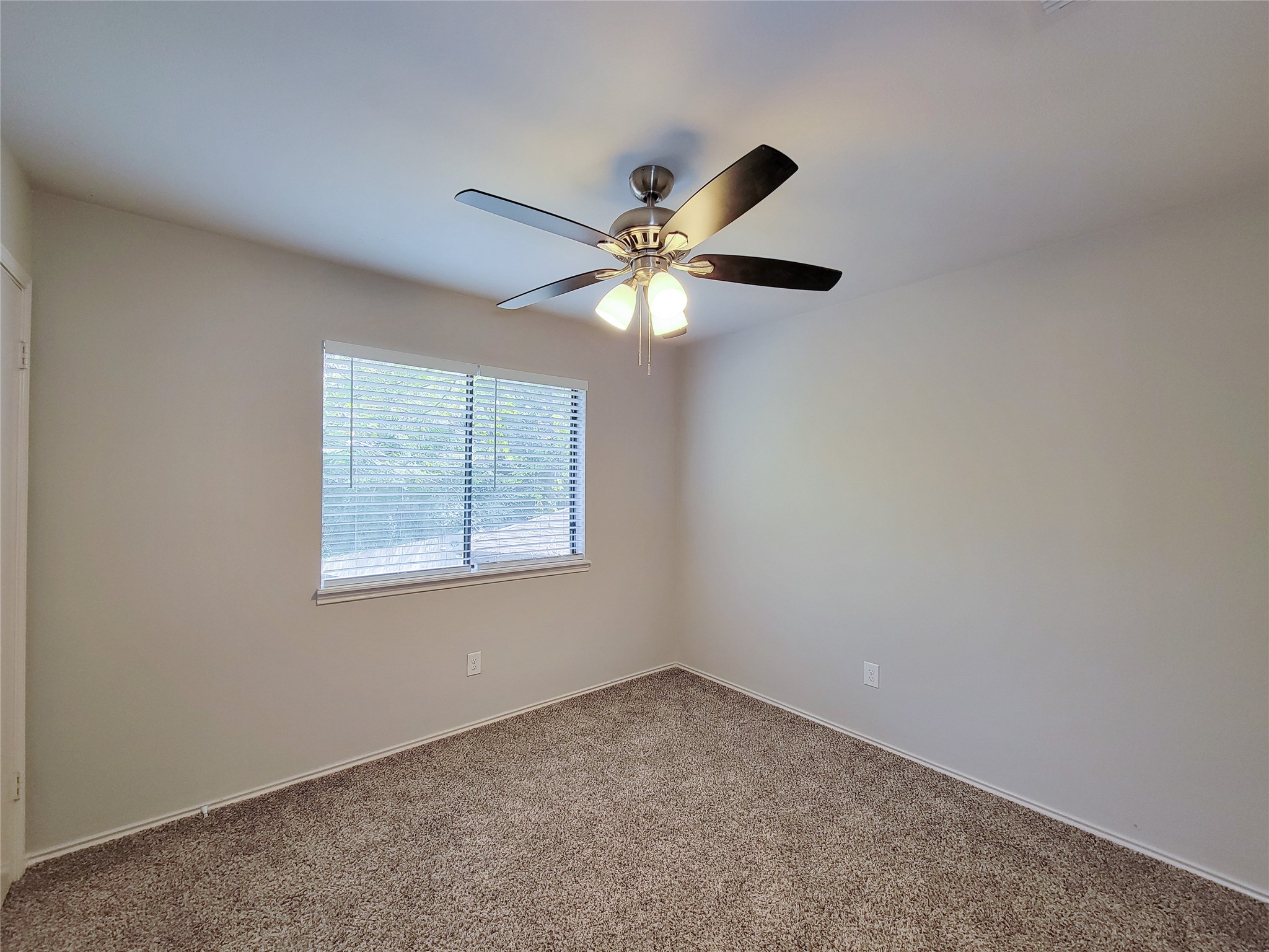 Cozy bedroom with plush carpet, neutral walls, and a ceiling fan, offering natural light through a well-sized window with blinds.