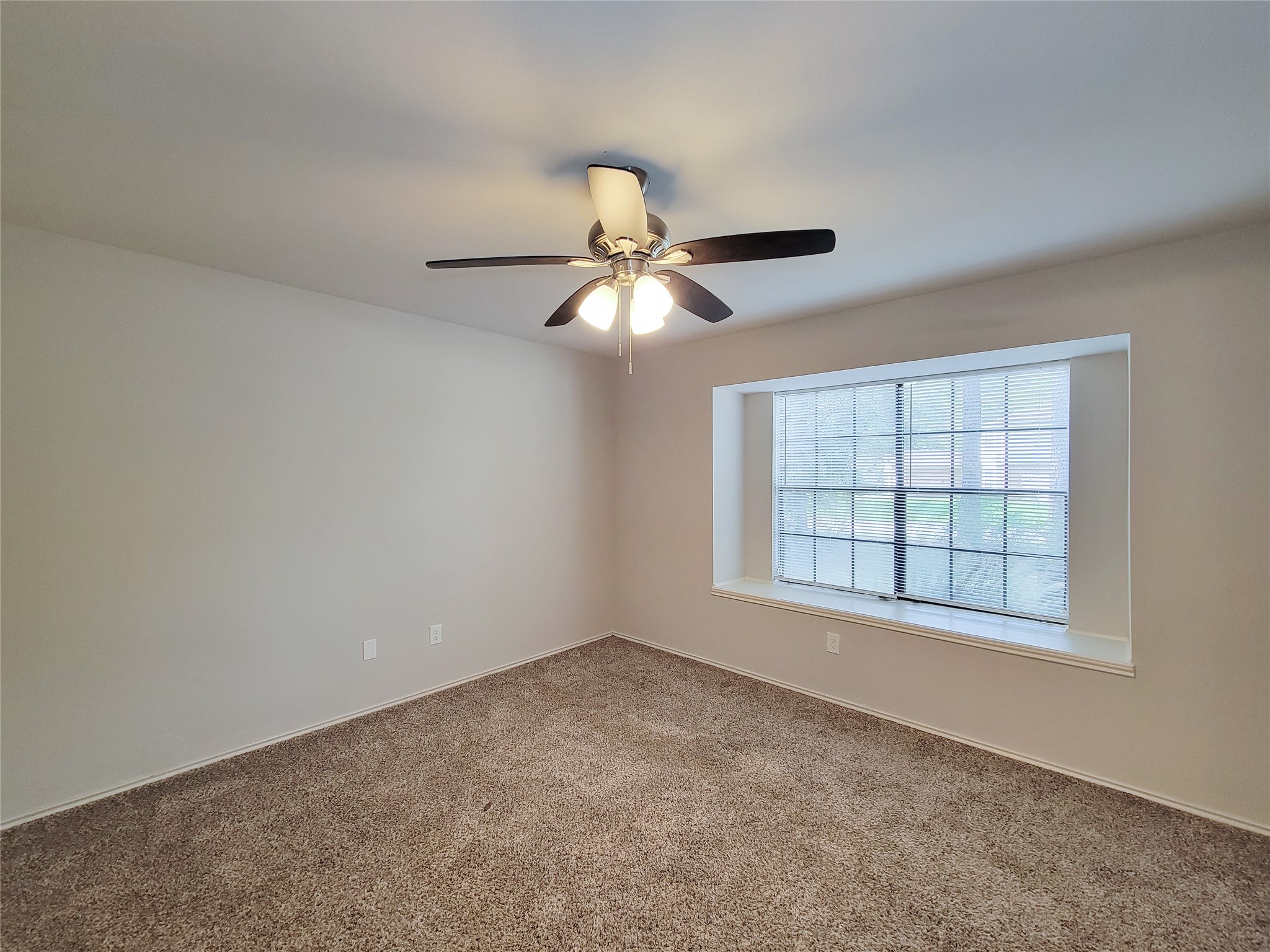 Spacious room featuring a large bay window, plush carpeting, and a ceiling fan for comfort and style.