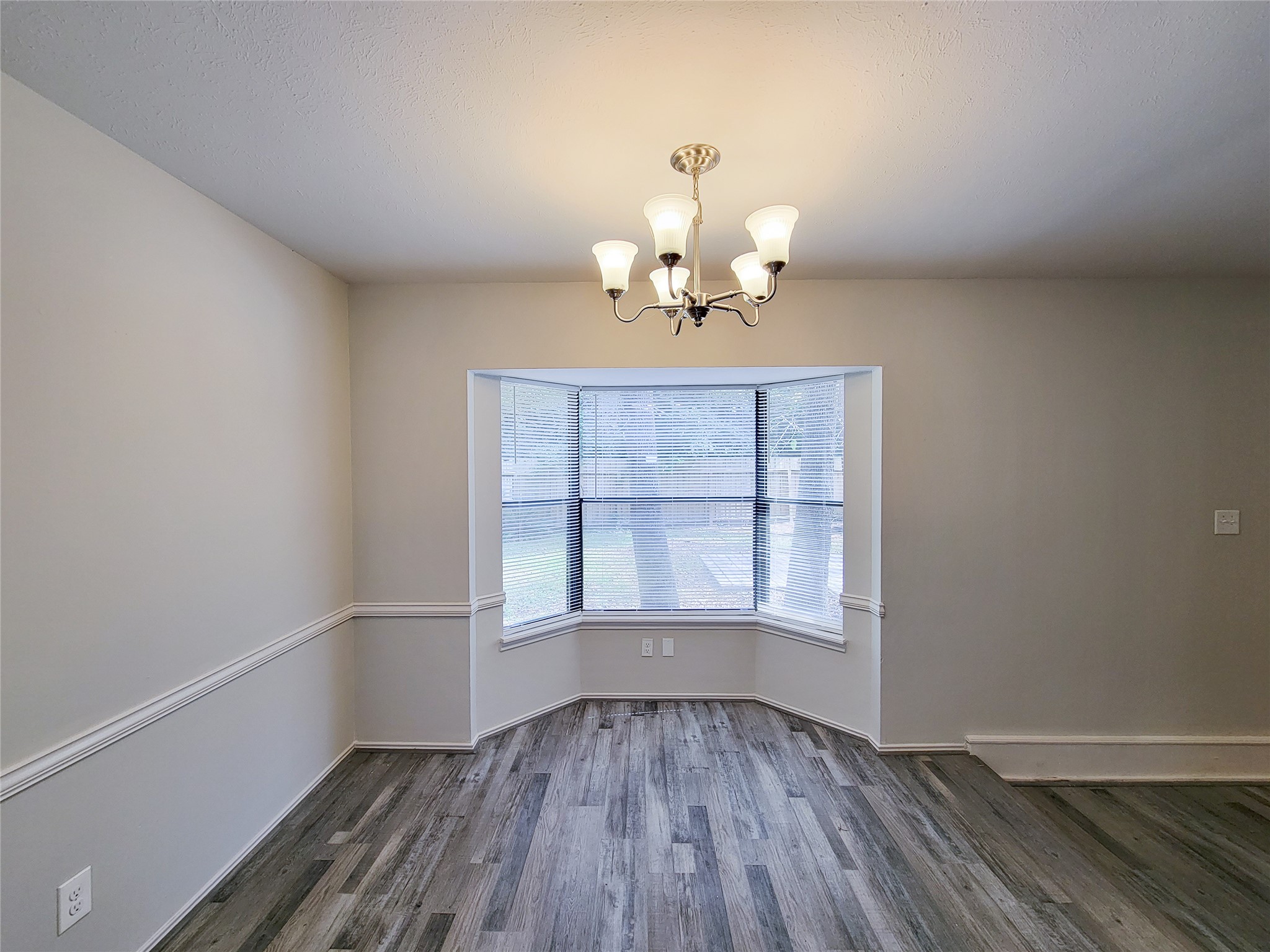 Bright dining area with a bay window, elegant chandelier, and stylish wood flooring.