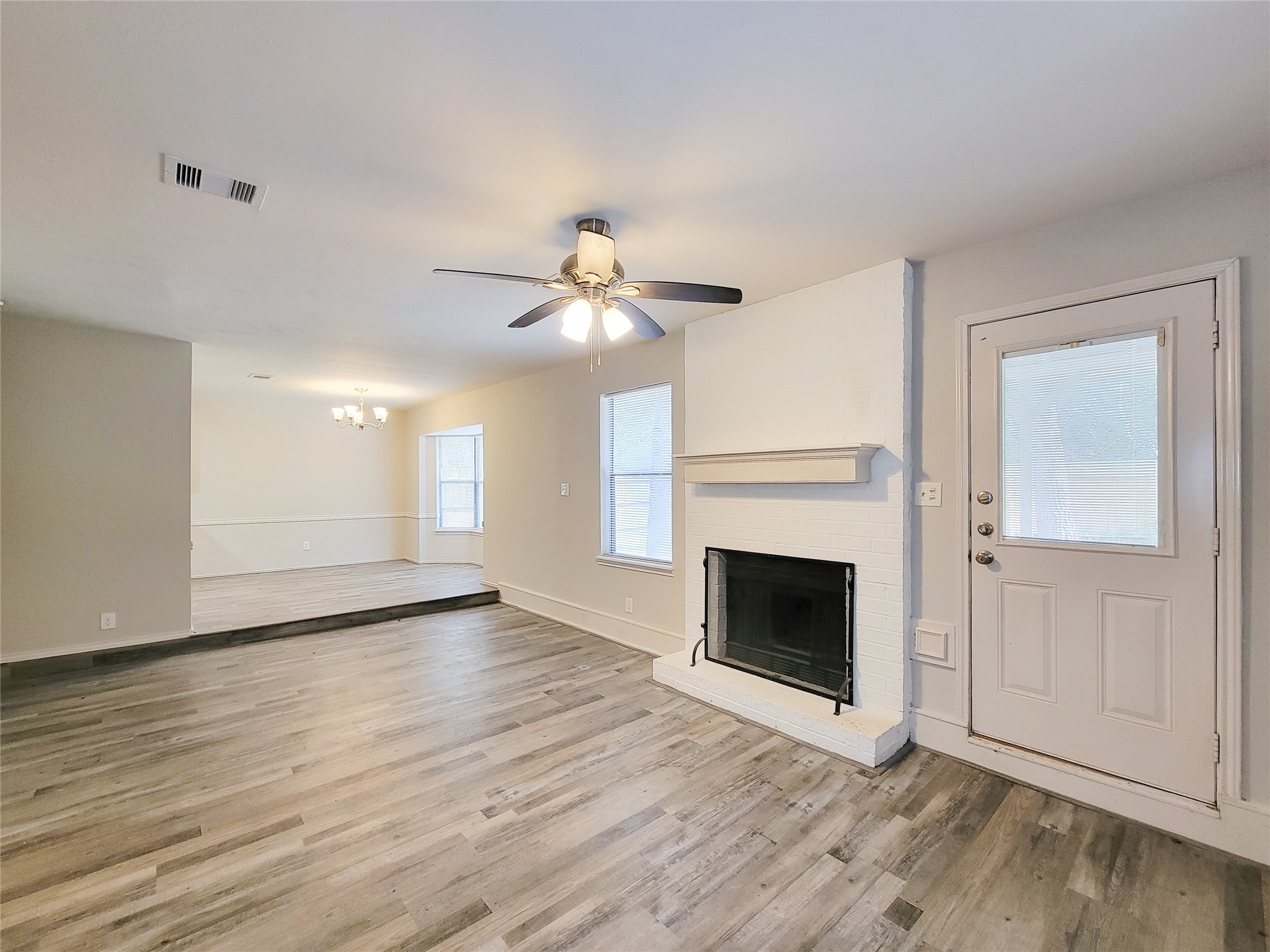 Spacious living area featuring laminate wood flooring, a cozy white brick fireplace, and abundant natural light, seamlessly flowing into an elevated dining space.