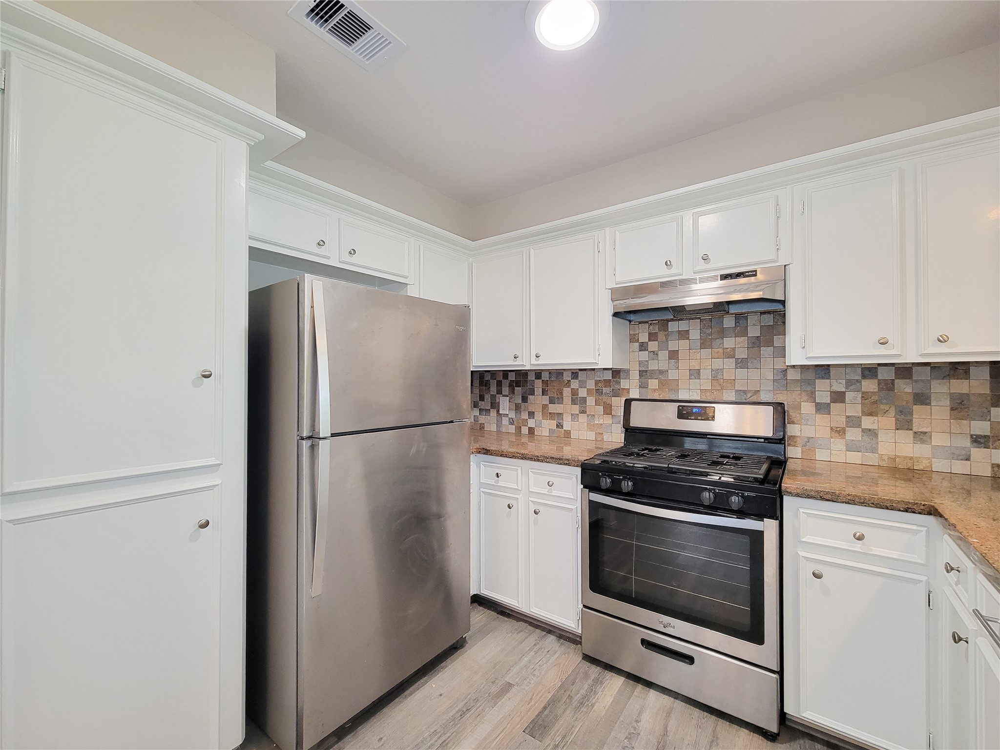 Charming kitchen with stainless steel appliances, ample white cabinetry, and a stylish mosaic tile backsplash.
