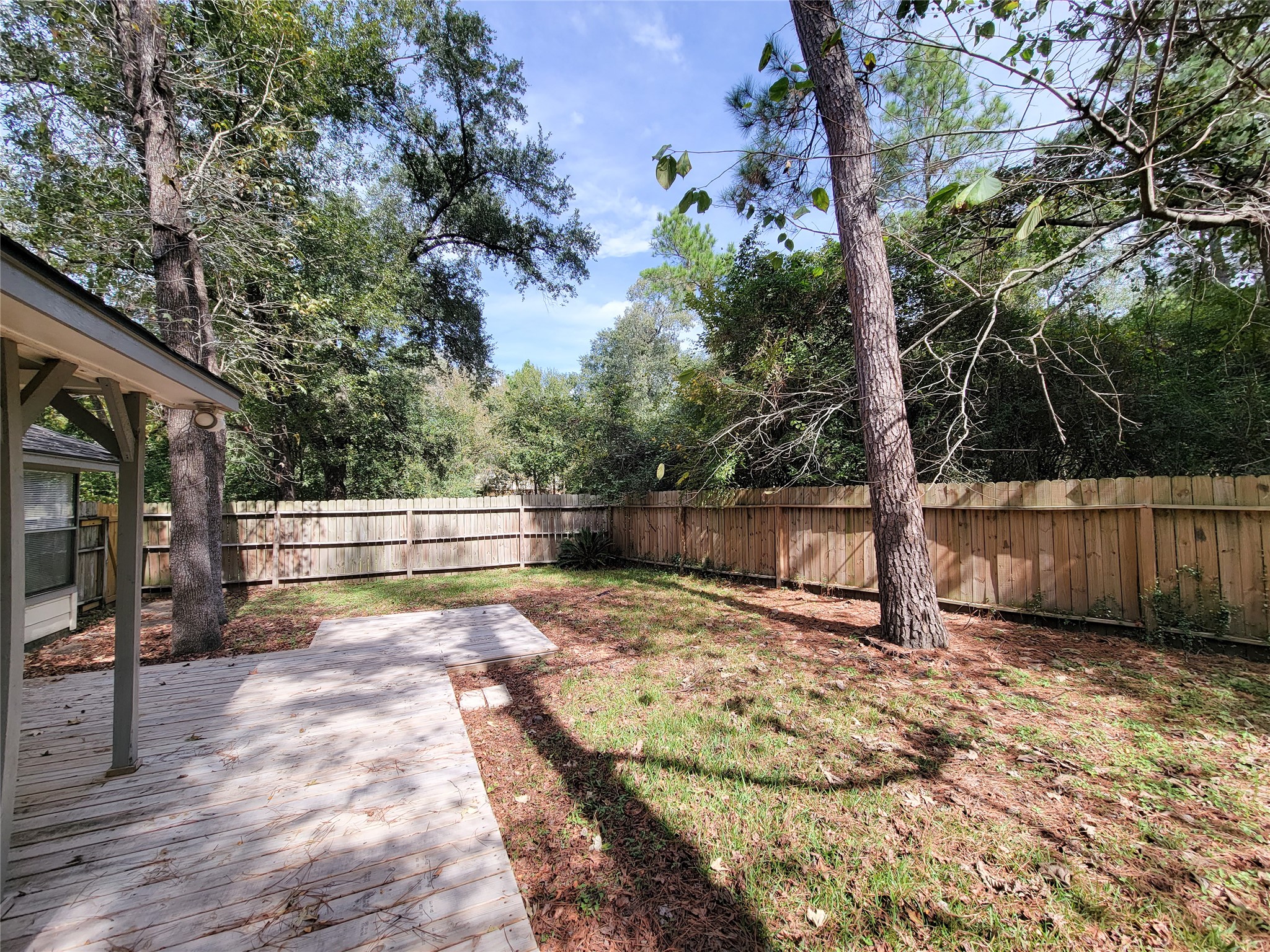 Spacious backyard with a wooden deck, surrounded by lush greenery and a privacy fence, perfect for outdoor relaxation.
