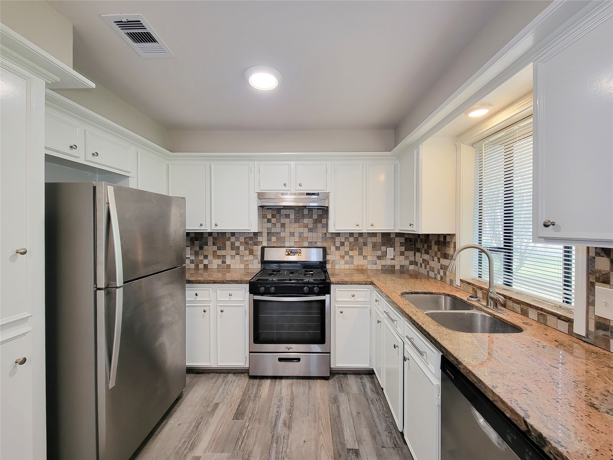 Charming kitchen with sleek stainless steel appliances, elegant granite countertops, and a stylish tile backsplash, enhanced by ample cabinet space and natural light from the window.