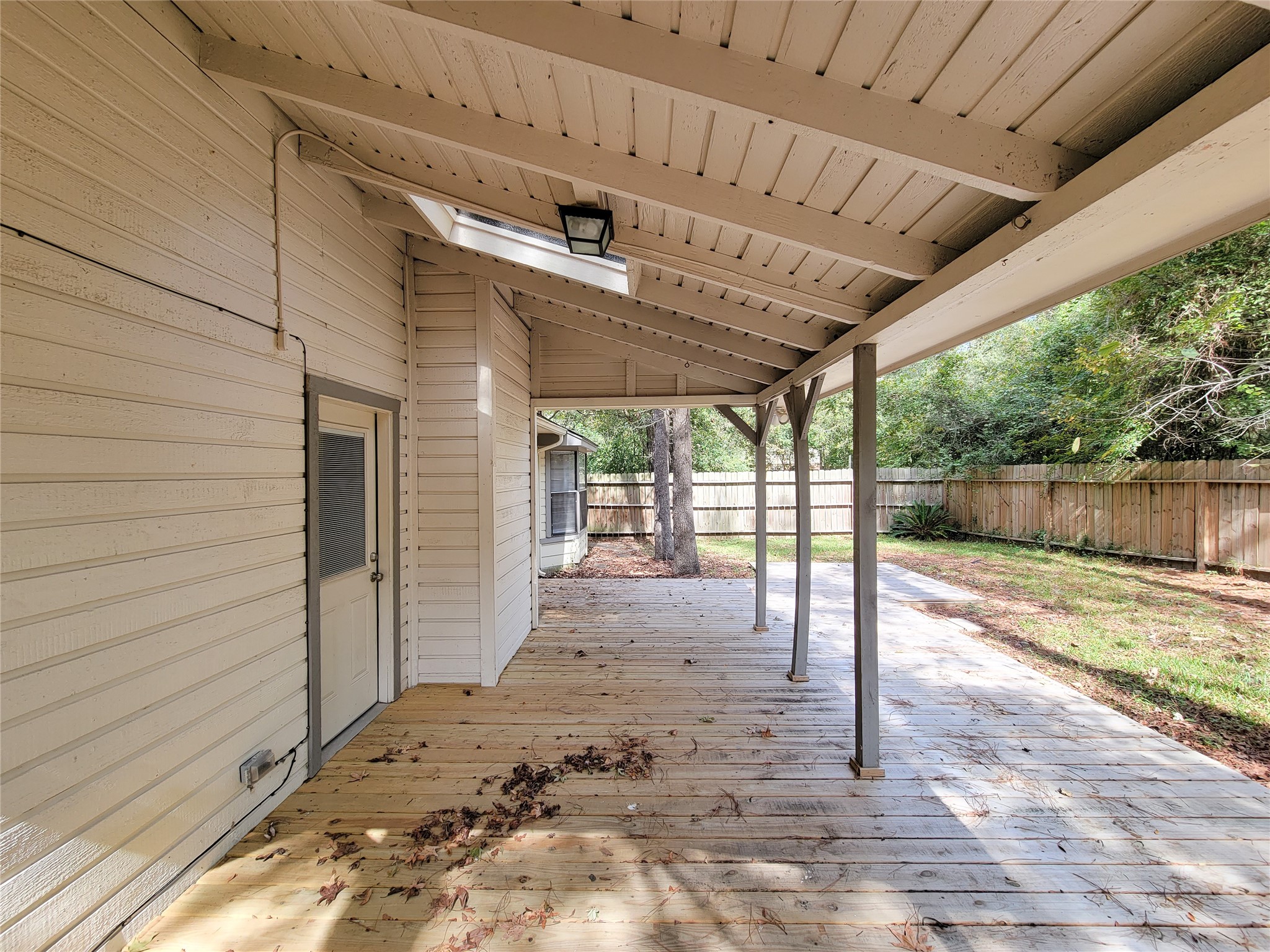 Spacious covered patio with wooden decking, perfect for outdoor relaxation, overlooking a private fenced backyard with lush greenery.