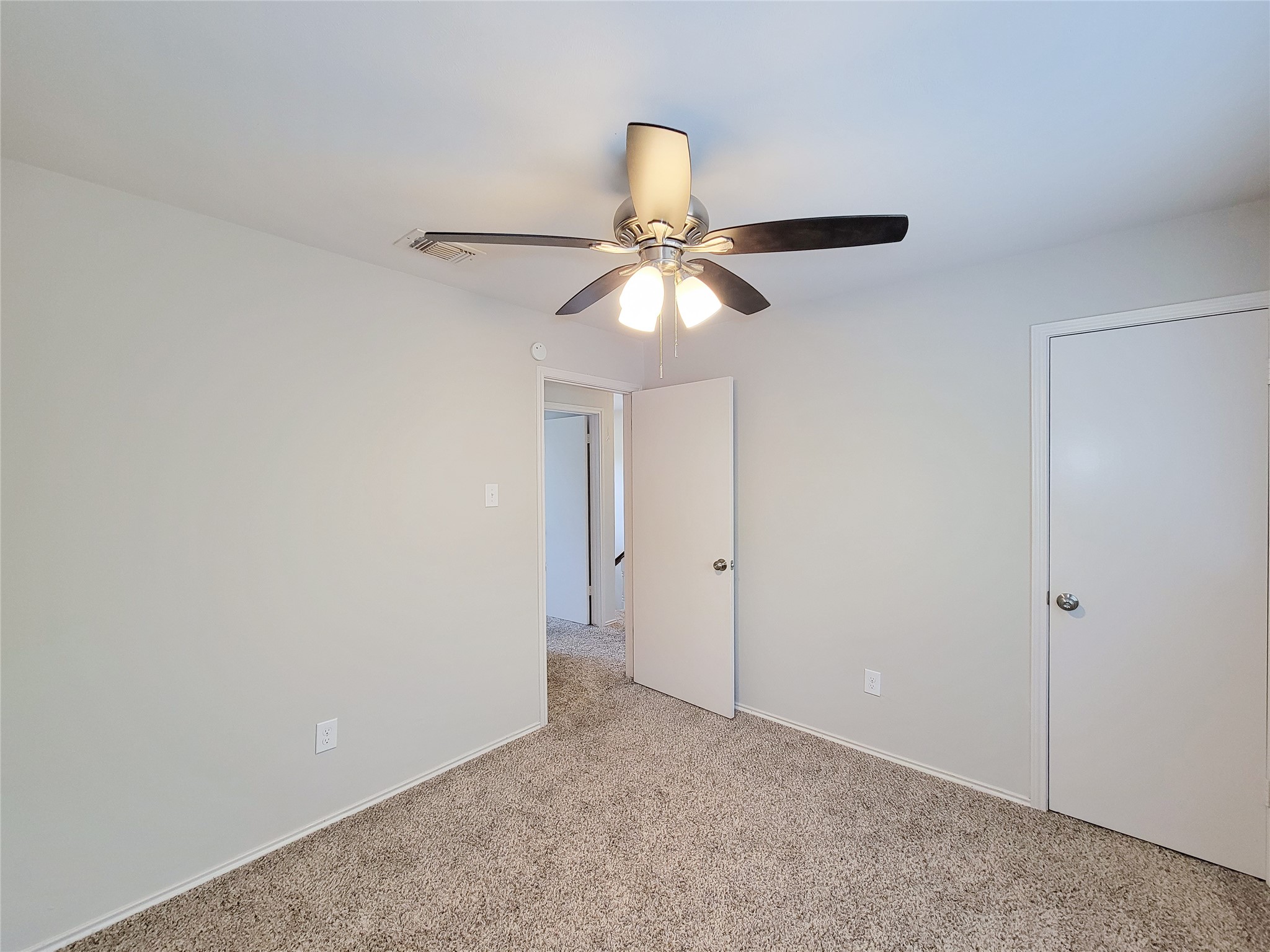 Bright bedroom with soft carpet, neutral walls, and a ceiling fan for comfort.