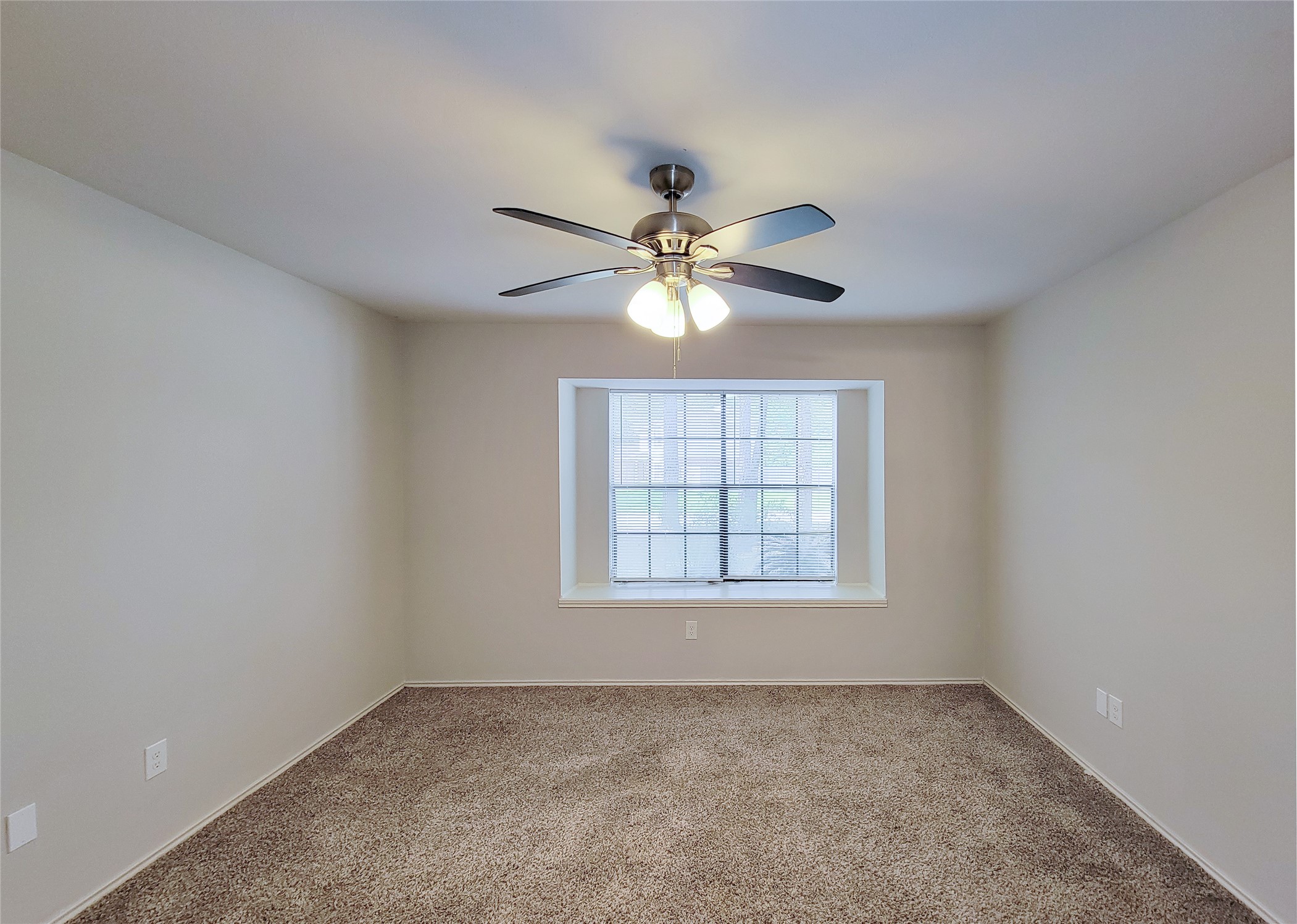 Spacious bedroom featuring plush carpet, neutral walls, a ceiling fan with light, and a large window offering natural light.