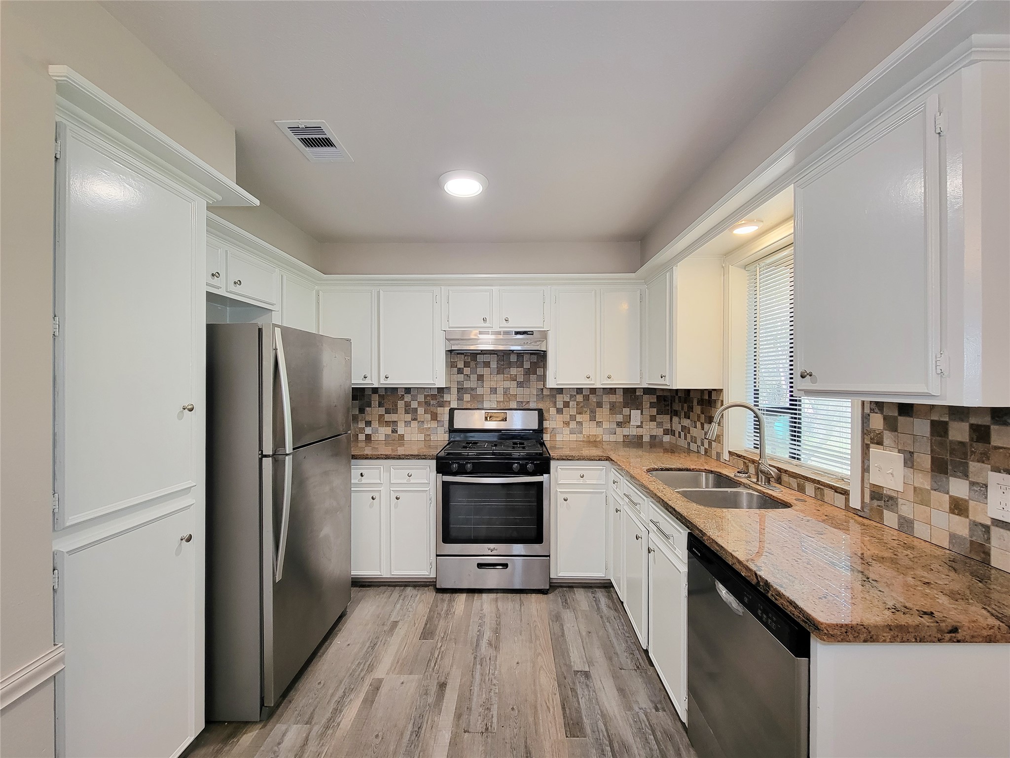 Charming kitchen with sleek stainless steel appliances, elegant granite countertops, and stylish mosaic tile backsplash, complemented by pristine white cabinetry and warm wood-look flooring.