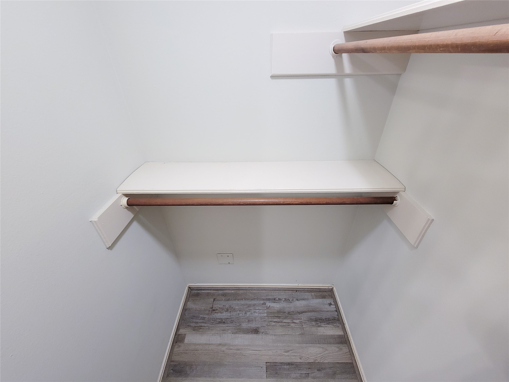 Spacious walk-in closet featuring dual hanging rods and a convenient built-in shelf, complemented by sleek wood flooring.
