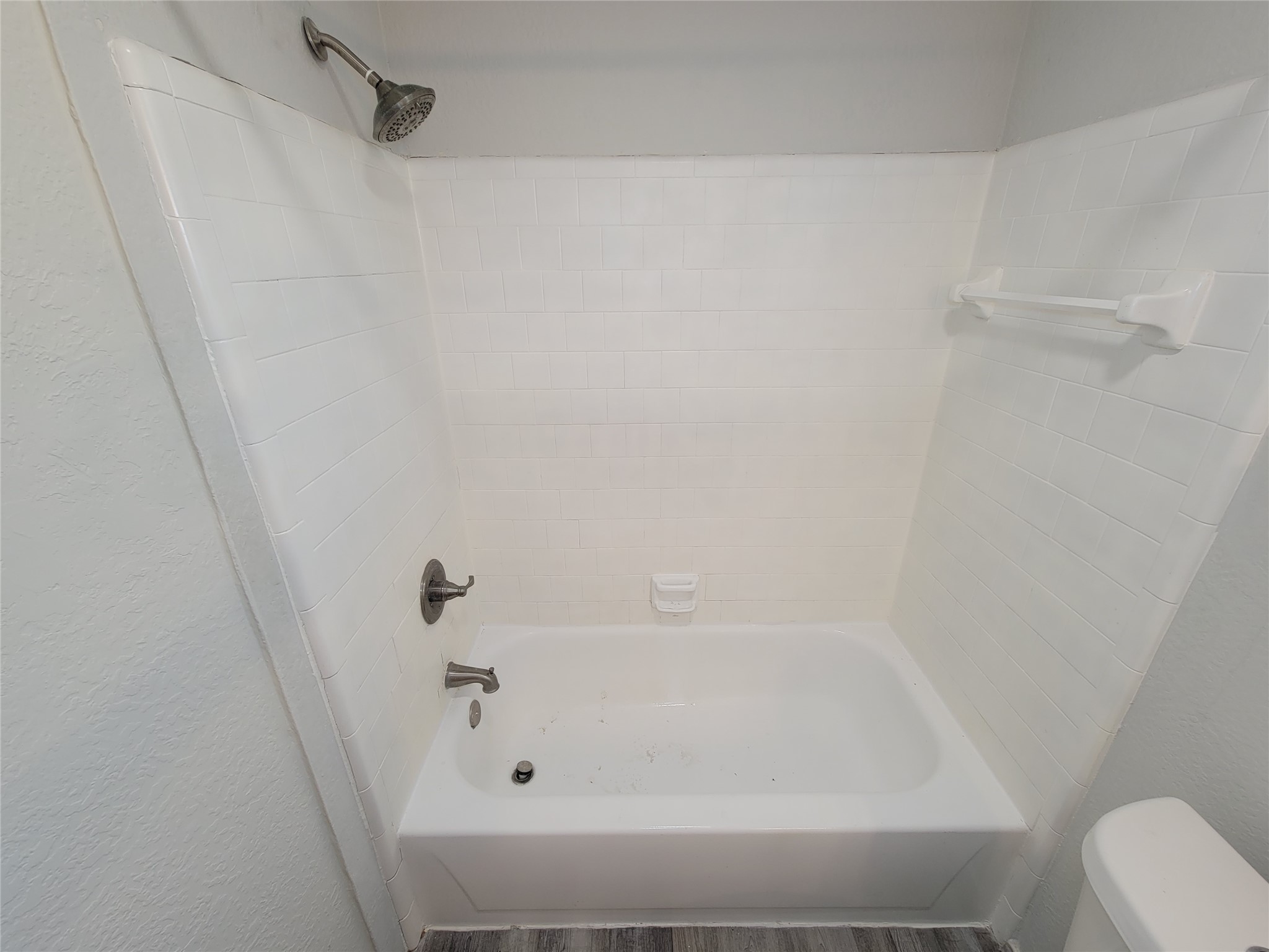 Bright and clean bathroom featuring a classic white tiled shower and tub combo, complemented by modern fixtures and neutral tones.