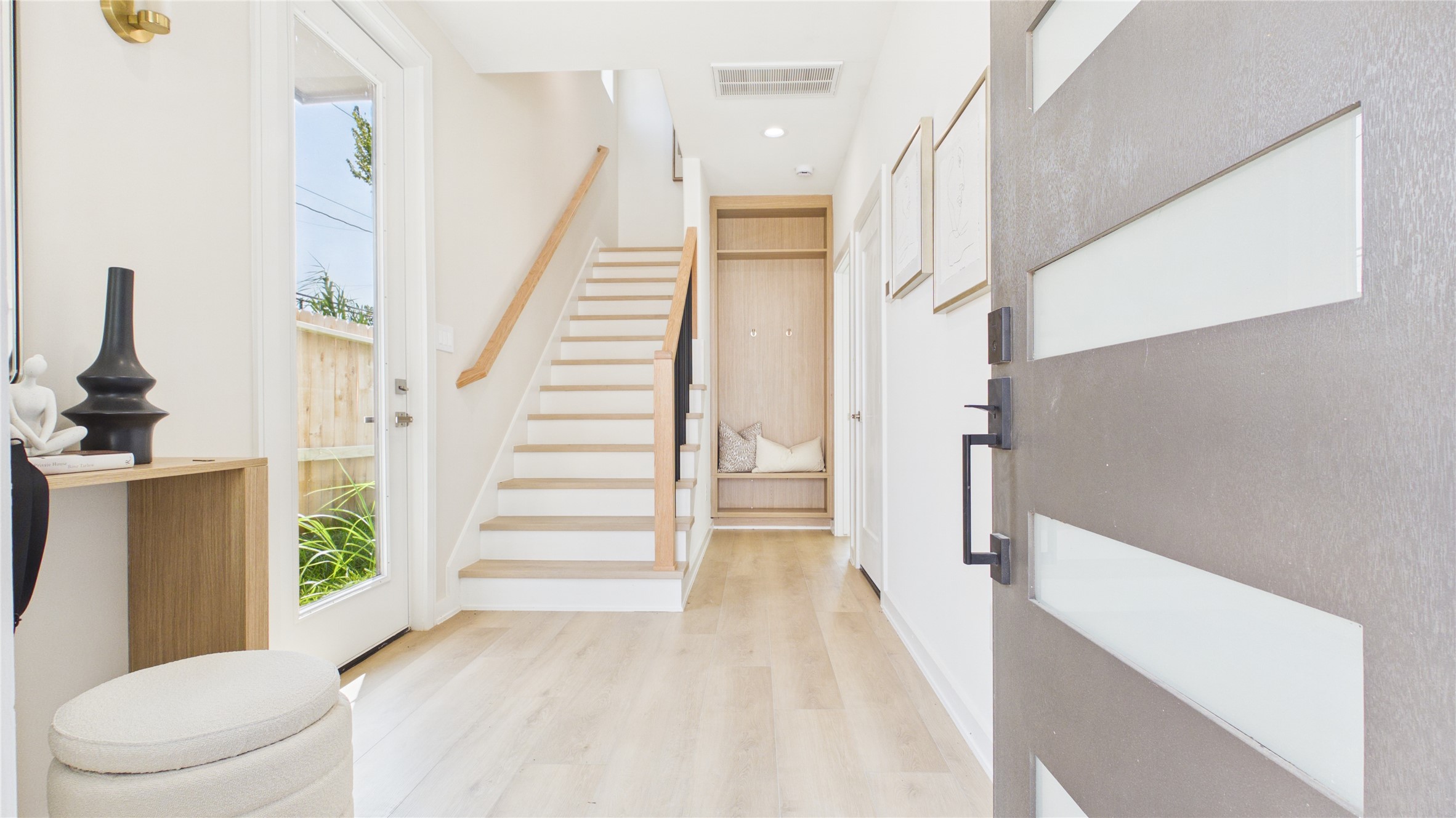 Bright and welcoming entryway featuring modern design, light wood flooring, and a stylish staircase, creating an inviting first impression.