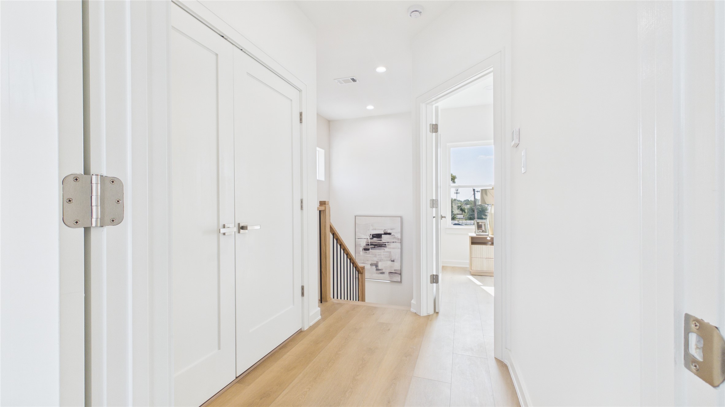 Bright and airy hallway featuring light wood flooring, modern recessed lighting, and access to multiple rooms including the laundry room, creating a welcoming and functional space.