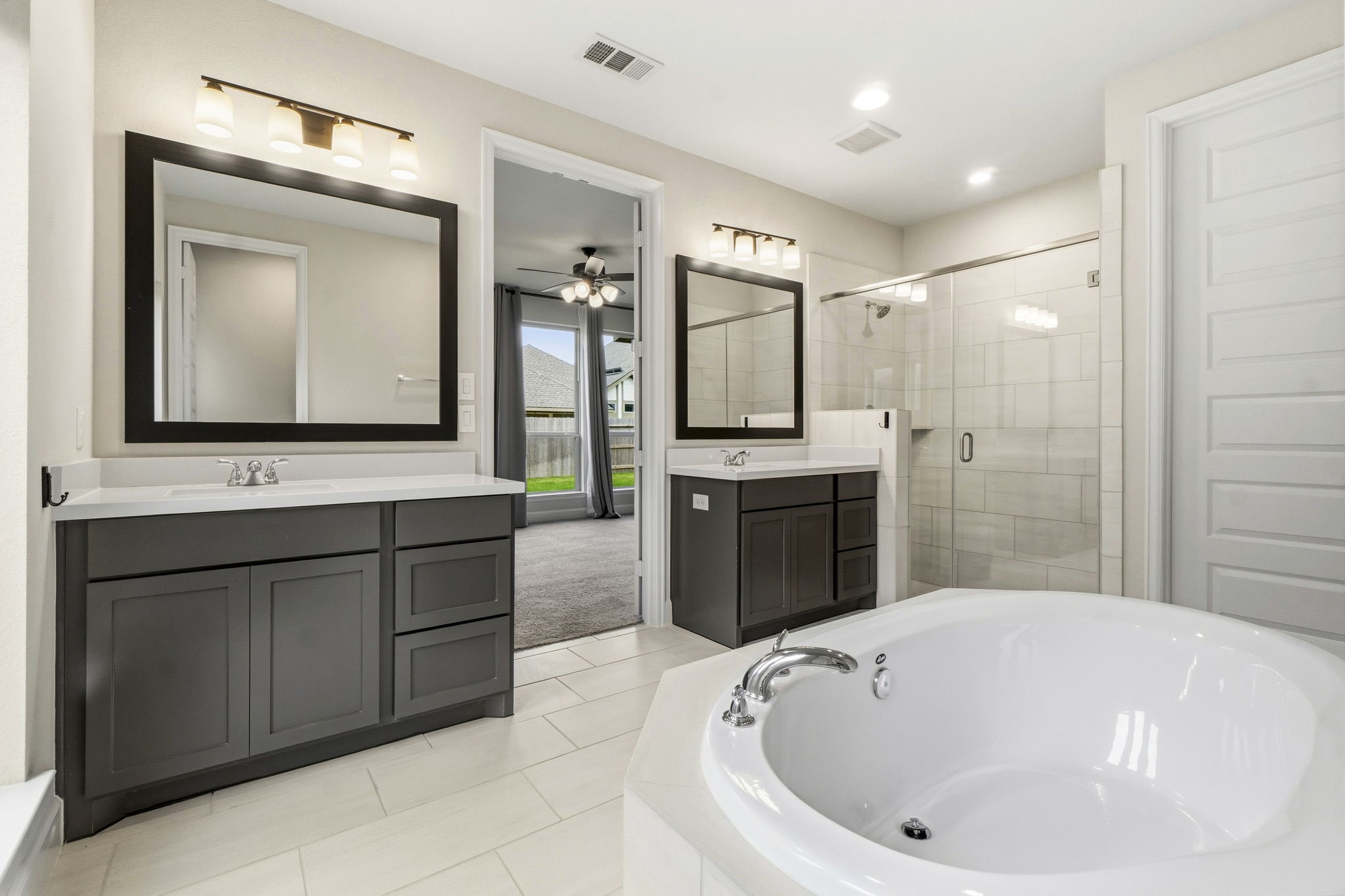 The spa-inspired primary bath features dual vanities with double sinks, a relaxing soaking tub, a separate glass-enclosed shower, and two spacious walk-in closets.
